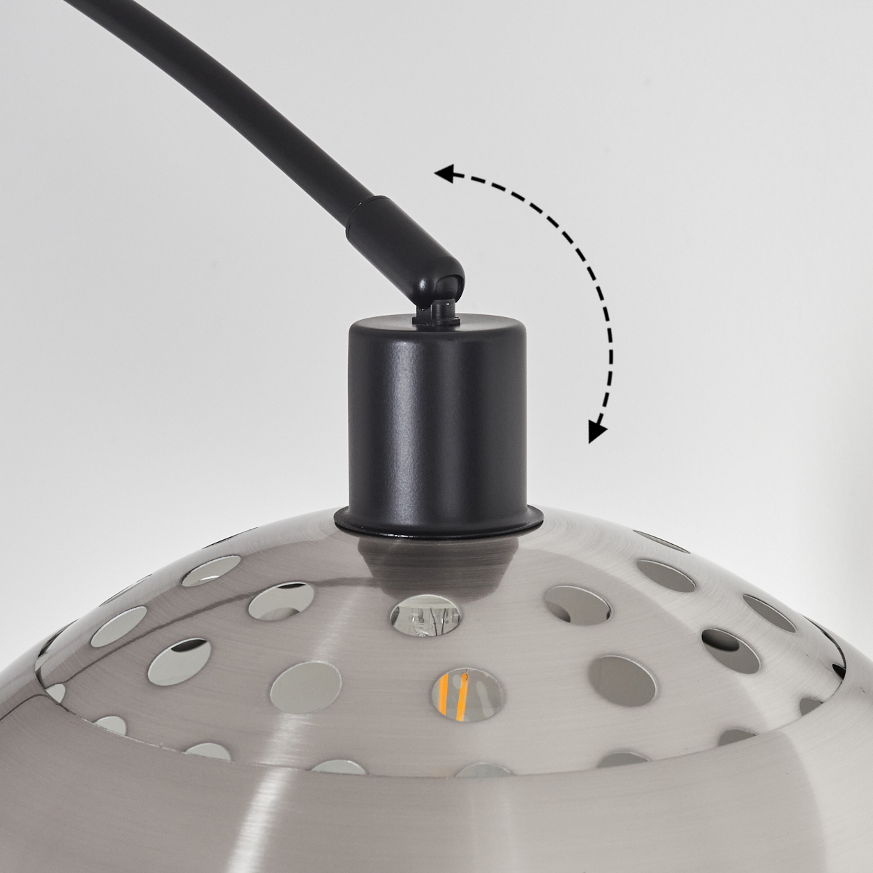 Nahaufnahme einer Lampe mit schwarzem Arm und silberfarbenem, perforiertem Schirm. Ein Pfeil zeigt die verstellbare Bewegung an.