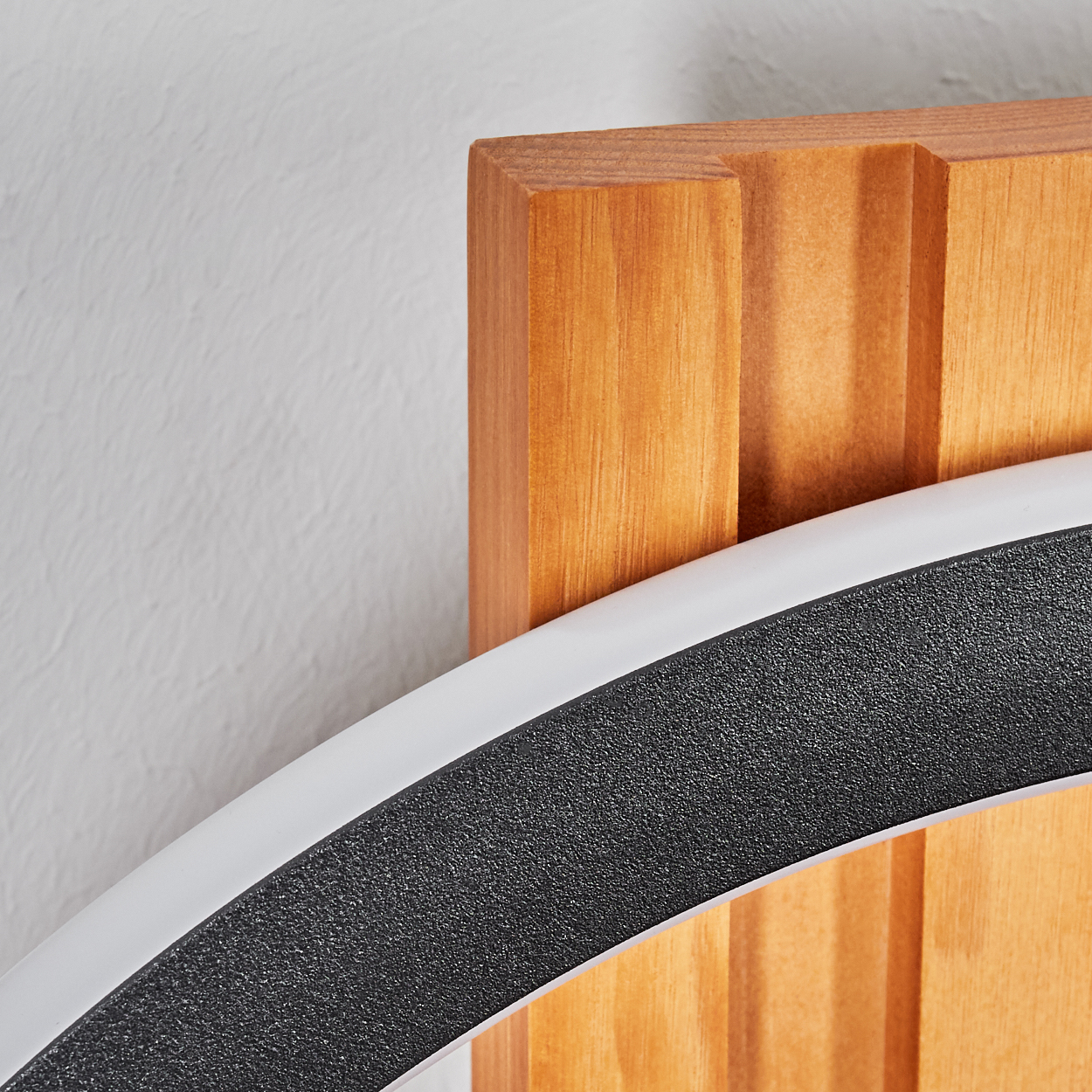 Nahaufnahme einer Holzstruktur mit schwarzer, strukturierter Oberfläche und einem weißen, gebogenen Element. Der Hintergrund ist eine weiße Wand.