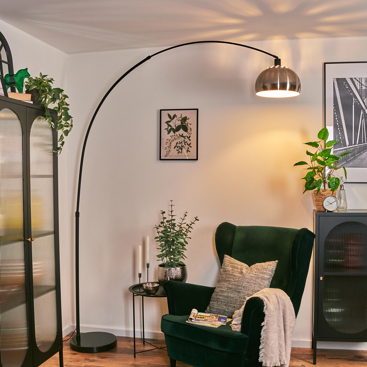 Ein modernes Wohnzimmer mit grünem Sessel, Stehlampe und dekorativen Pflanzen. Eine Zeitschrift und eine Decke liegen auf dem Stuhl.