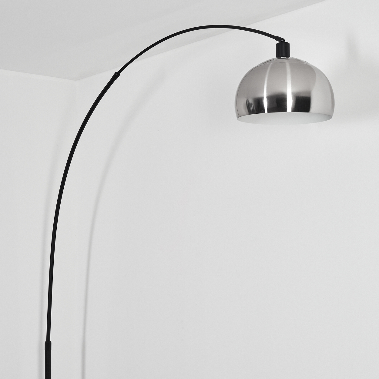 Eine moderne Bogenstehlampe mit silbernem Kuppel-Schirm. Der schwarze Bogen erstreckt sich vom Boden zur weißen Wand in der Ecke.