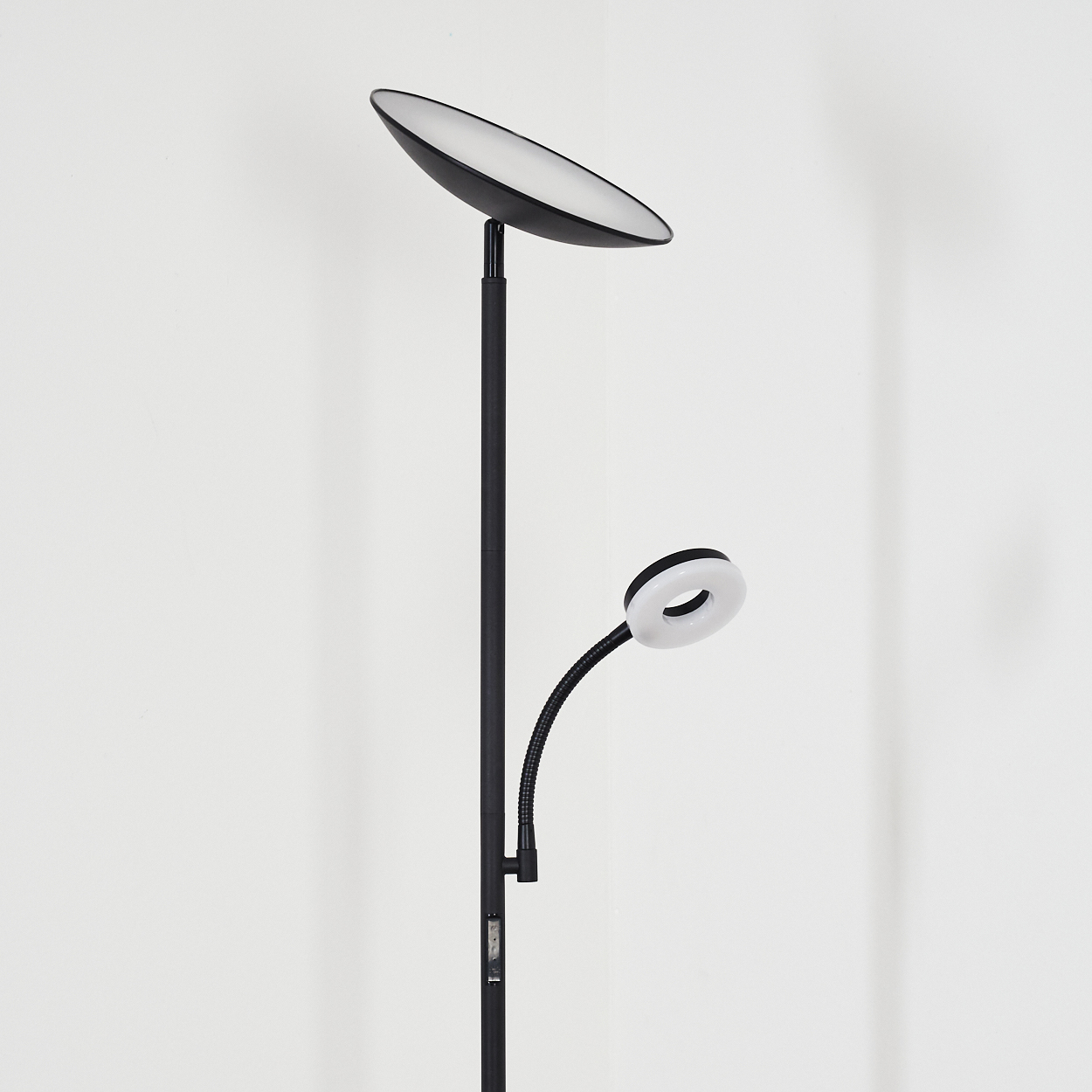 Eine schwarze Stehlampe mit zwei Lichtern, einem großen ovalen Oberlicht und einem Ringlicht an einem flexiblen Arm, vor einer weißen Wand.