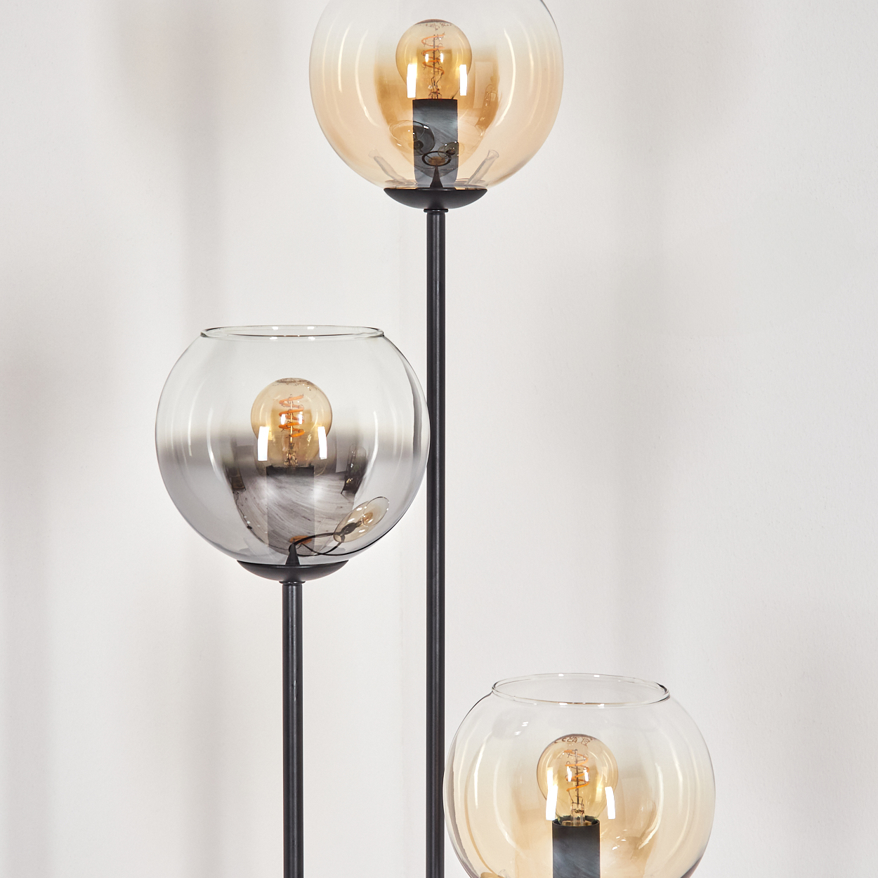 Eine moderne Stehlampe mit drei kugelförmigen Schirmen. Die oberen und unteren Schirme sind bernsteinfarben, der mittlere ist grau.