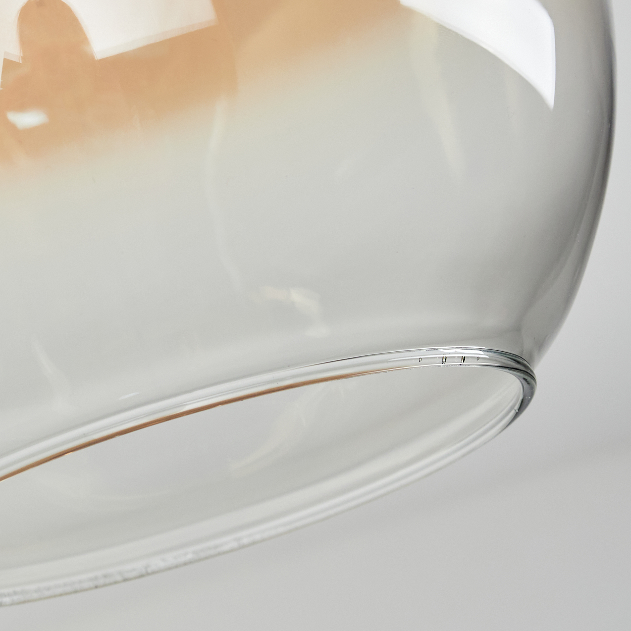 Nahaufnahme eines durchsichtigen Glasschirms. Der obere Teil hat einen hellbraunen Farbton. Der Boden ist klar. Ein weißer Hintergrund ist sichtbar.