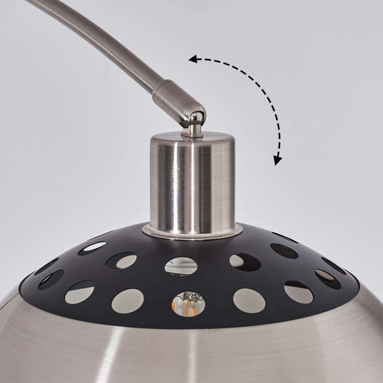 Nahaufnahme einer Lampe. Sie hat eine gebürstete Metalloberfläche mit einem schwarzen Oberteil mit ovalen Ausschnitten. Ein gebogener Arm erstreckt sich von oben.