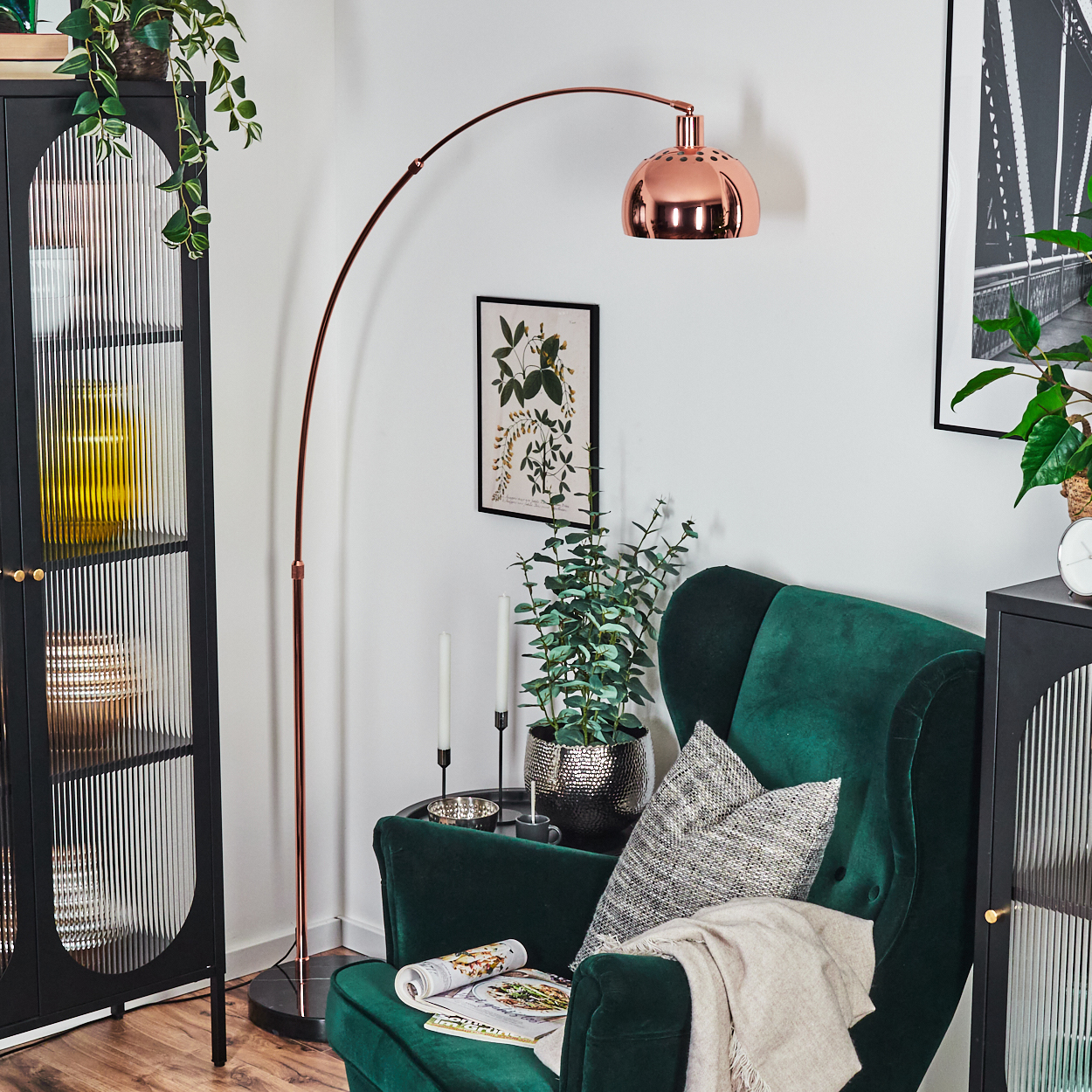 Ein Raum mit grünem Sessel, Kupferlampe, schwarzem Schrank und Pflanzen. Auf dem Stuhl liegt eine Zeitschrift.