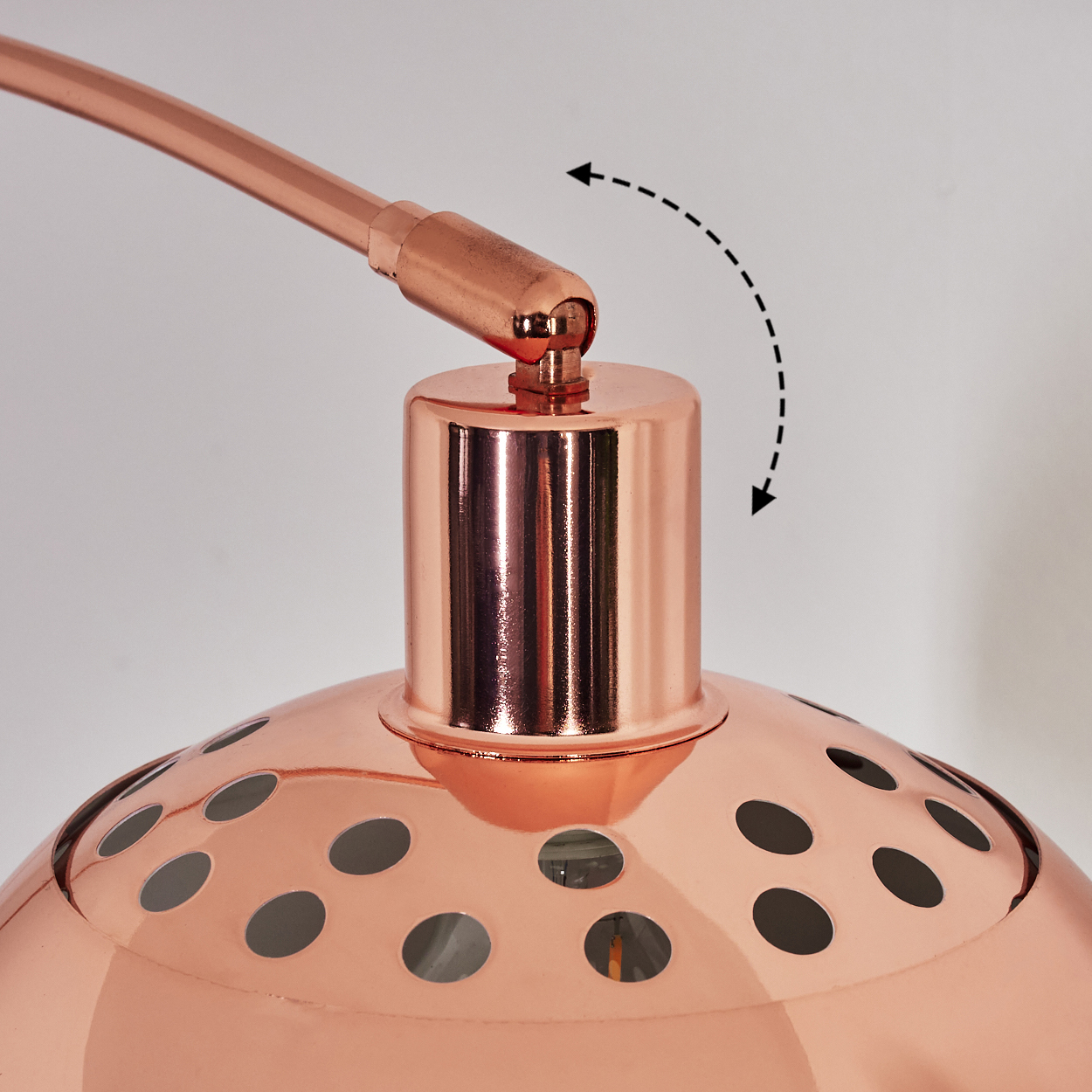 Nahaufnahme einer Kupferlampe. Die Lampe hat einen runden Schirm mit Löchern und einen gebogenen Arm. Pfeile deuten auf eine Drehbewegung hin.