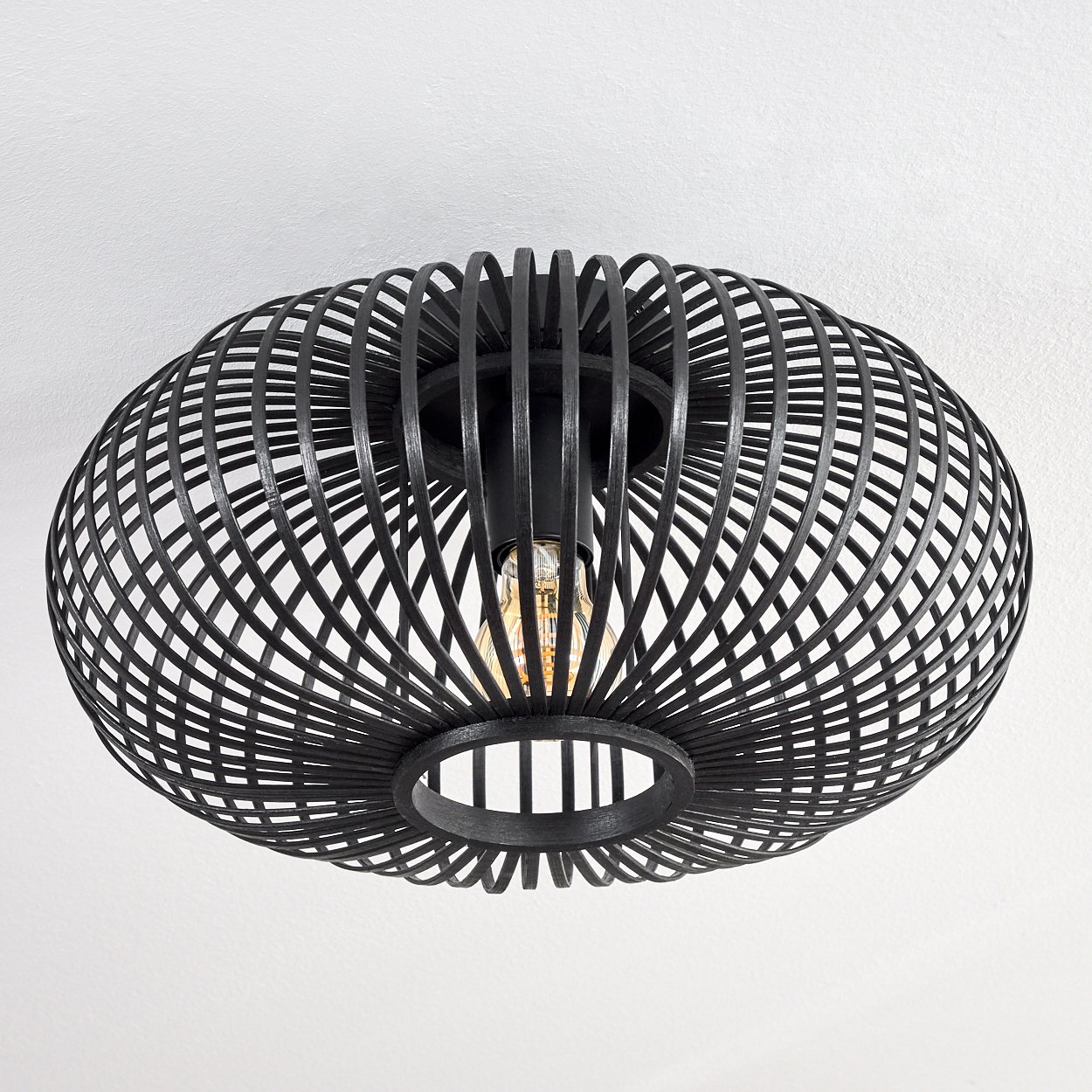 Schwarze, käfigartige Deckenlampe mit sichtbarer Glühbirne, an einer weißen Decke montiert. Das Design ist modern und geometrisch.