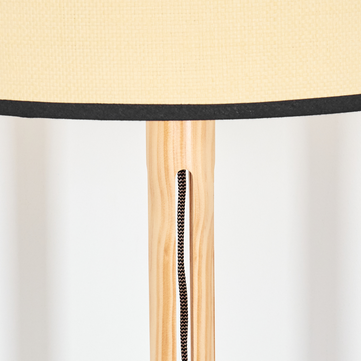 Nahaufnahme einer Lampe. Beiger Lampenschirm mit schwarzem Rand. Heller Holzständer mit schwarzem Kabel, weißer Hintergrund.