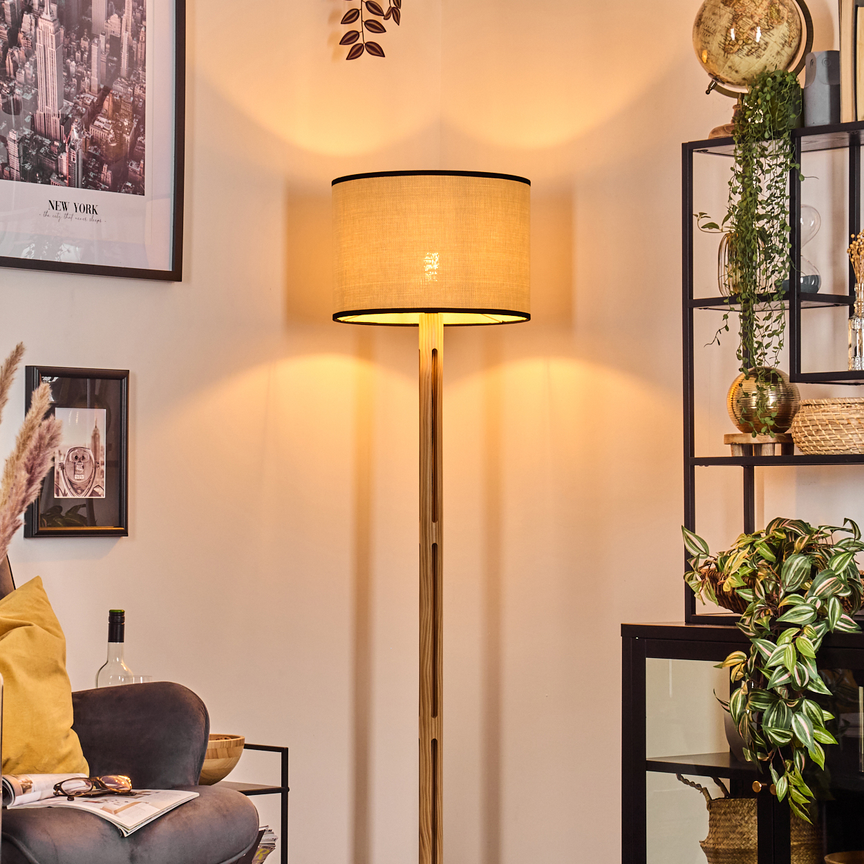 Eine Stehlampe steht in einem Raum mit einem New York-Bild und einem Regal mit Pflanzen. Die Lampe beschattet den Raum.