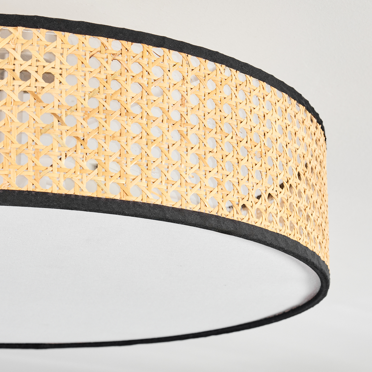 Nahaufnahme einer Deckenlampe. Sie hat einen Schirm aus gewebtem Rattan mit schwarzem Rand und weißem Innenraum.