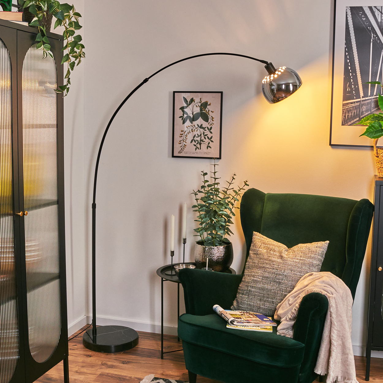 Ein grüner Sessel mit Kissen und Decke, eine schwarze Lampe, ein Schrank und ein Beistelltisch mit Pflanzen und Kerzen.