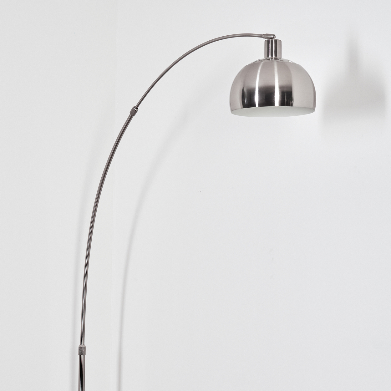 Eine moderne, silberne Bogen-Stehlampe vor einer weißen Wand. Die Lampe hat einen gebogenen Arm und einen kuppelförmigen Schirm.