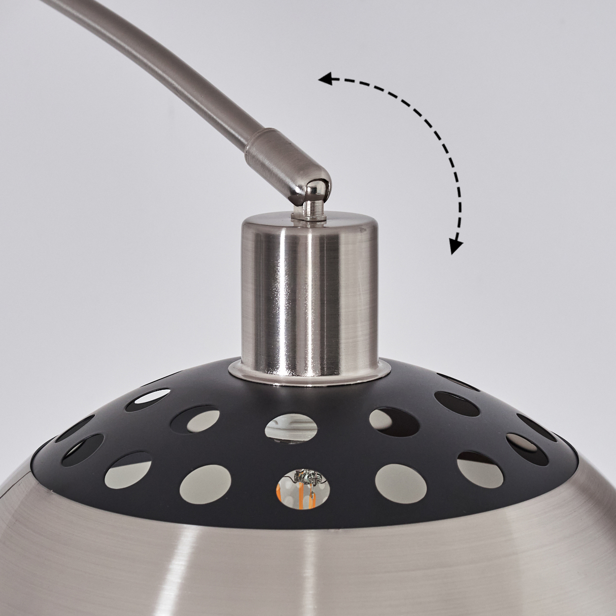 Nahaufnahme einer Lampe. Sie hat ein metallisches Finish und einen schwarzen Schirm mit Löchern. Ein Pfeil zeigt die Verstellbarkeit an.