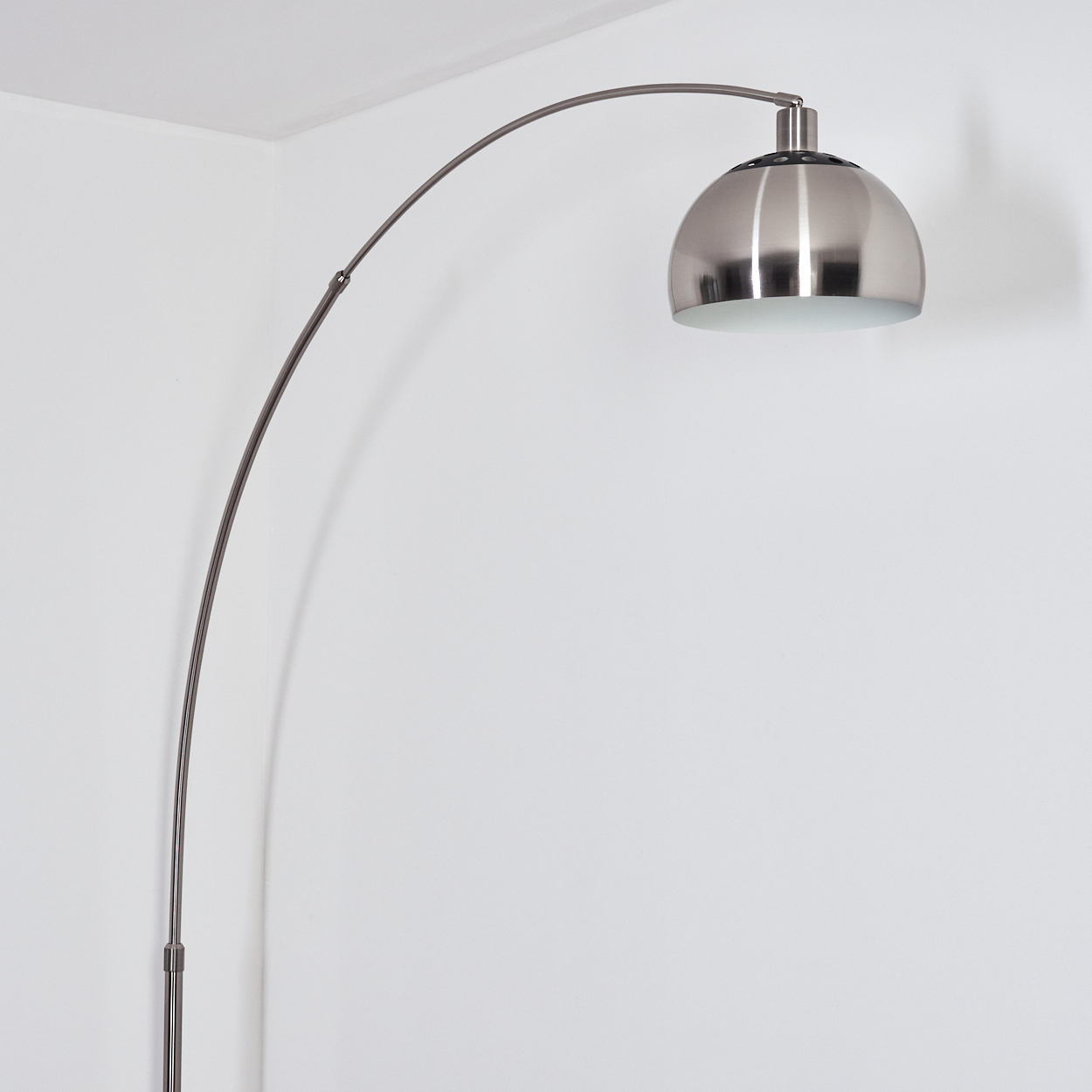 Eine moderne silberne Bogenstehlampe steht vor einer weißen Wand. Die Lampe hat einen gebogenen Arm und einen kuppelförmigen Kopf.
