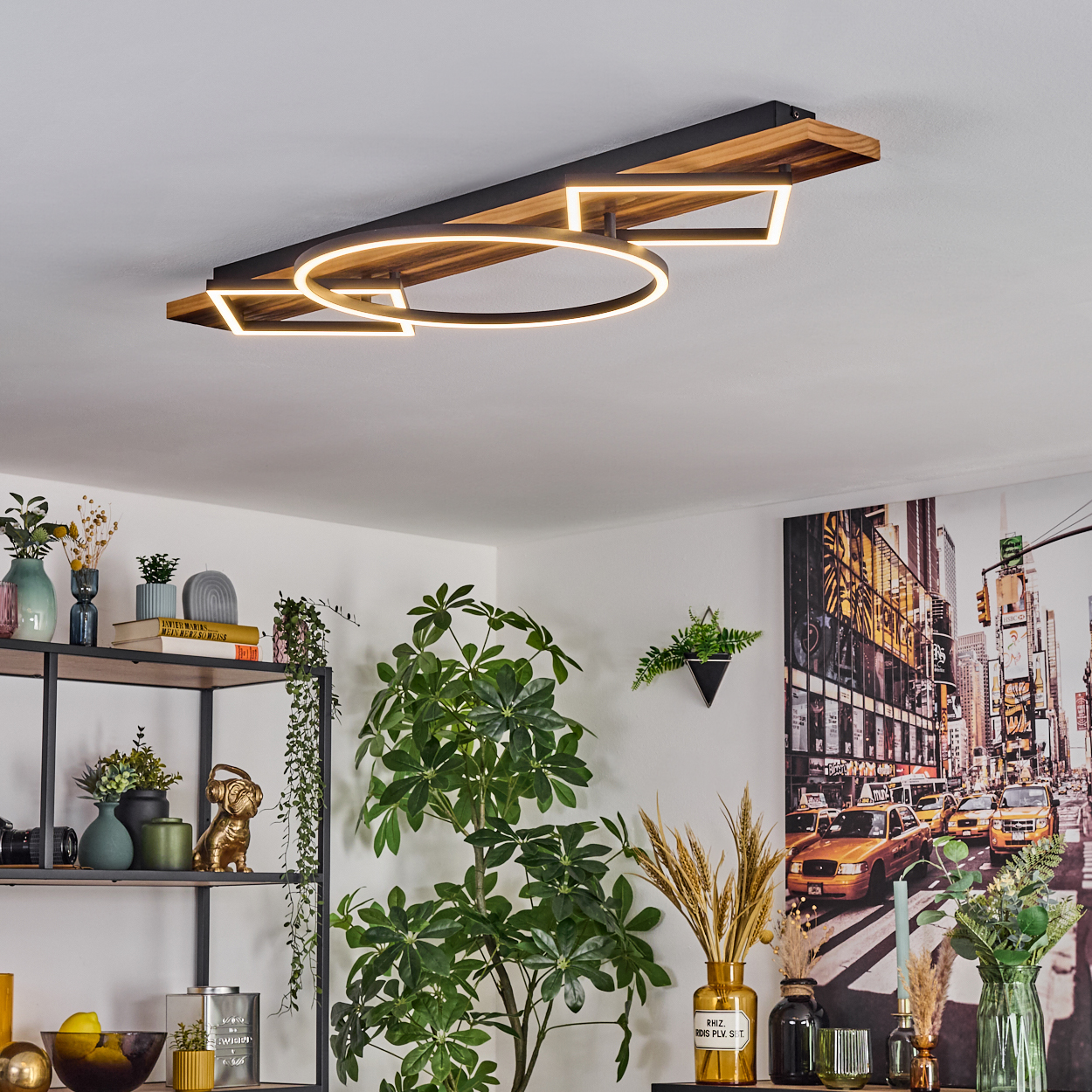 Eine moderne Deckenleuchte mit Holz- und schwarzem Design. Pflanzen und ein Regal mit Dekorationen sind im Vordergrund. Ein New York-Bild an der Wand.