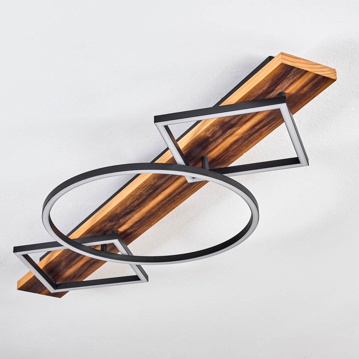 Eine moderne Deckenleuchte mit Holzsockel, geometrischen schwarzen Rahmen und einem kreisförmigen Licht. Der Hintergrund ist eine weiße Decke.