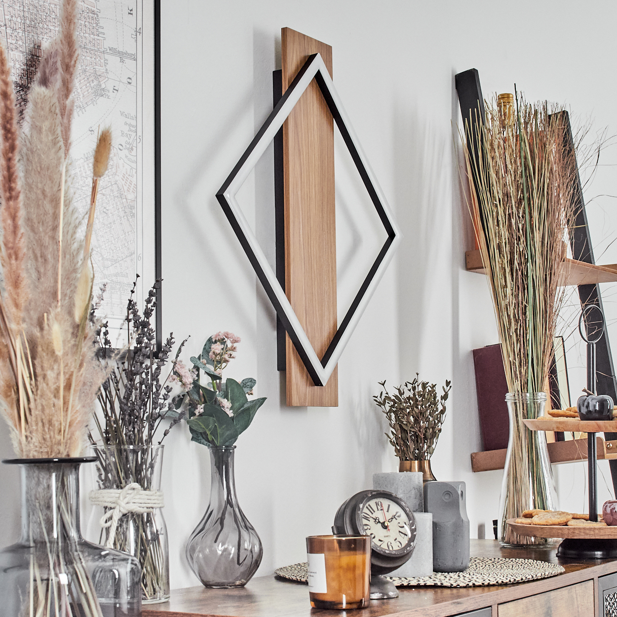 Ein Raum mit einem Holztisch. Vasen mit Pflanzen und Blumen, eine Uhr, eine Kerze und eine Wanddekoration.
