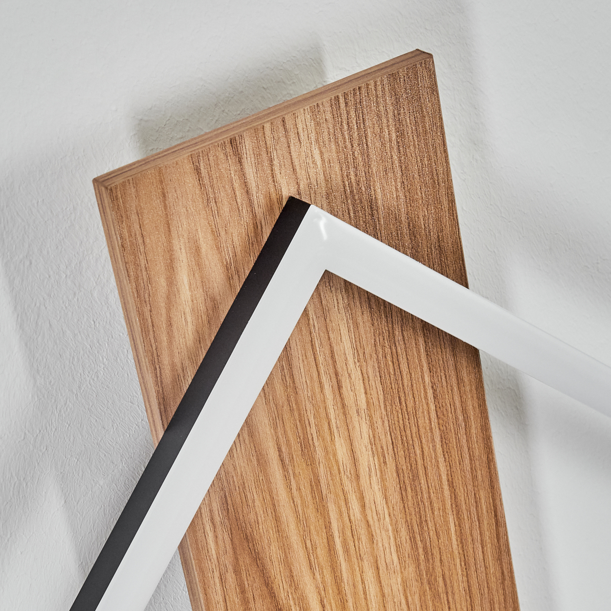 Holzbrett mit einem weiß-schwarzen Objekt. Der Hintergrund ist eine weiße, strukturierte Wand.