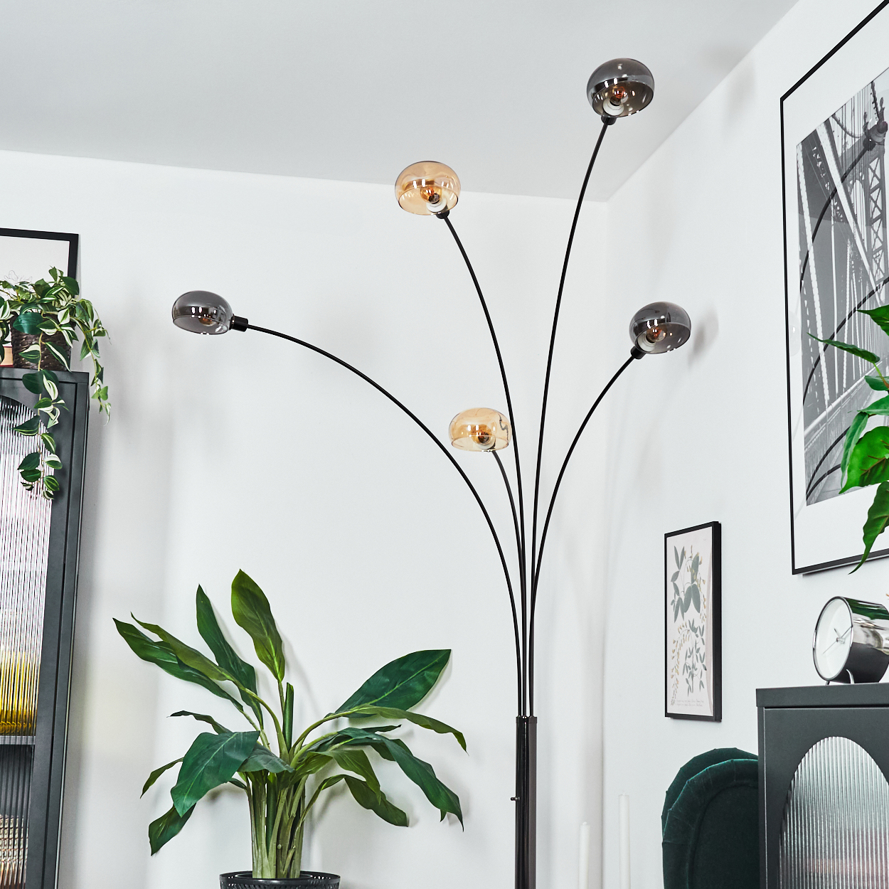 Eine moderne Stehlampe mit fünf Kugelleuchten. Eine Topfpflanze befindet sich im Vordergrund, und Kunstwerke hängen an der weißen Wand.