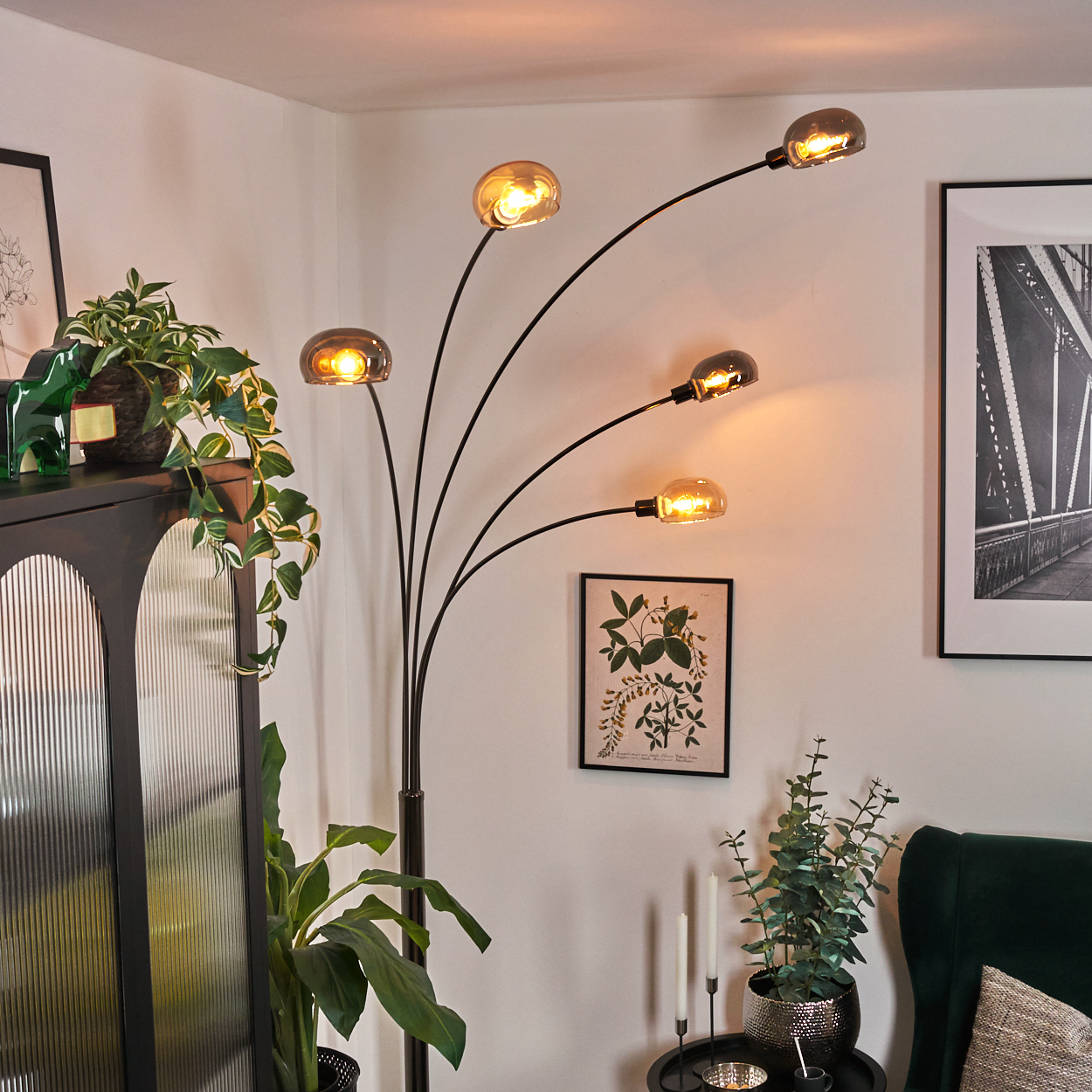 Ein modernes Wohnzimmer mit einer schwarzen Stehlampe mit fünf Glühbirnen. Pflanzen und gerahmte Kunstwerke schmücken den Raum.