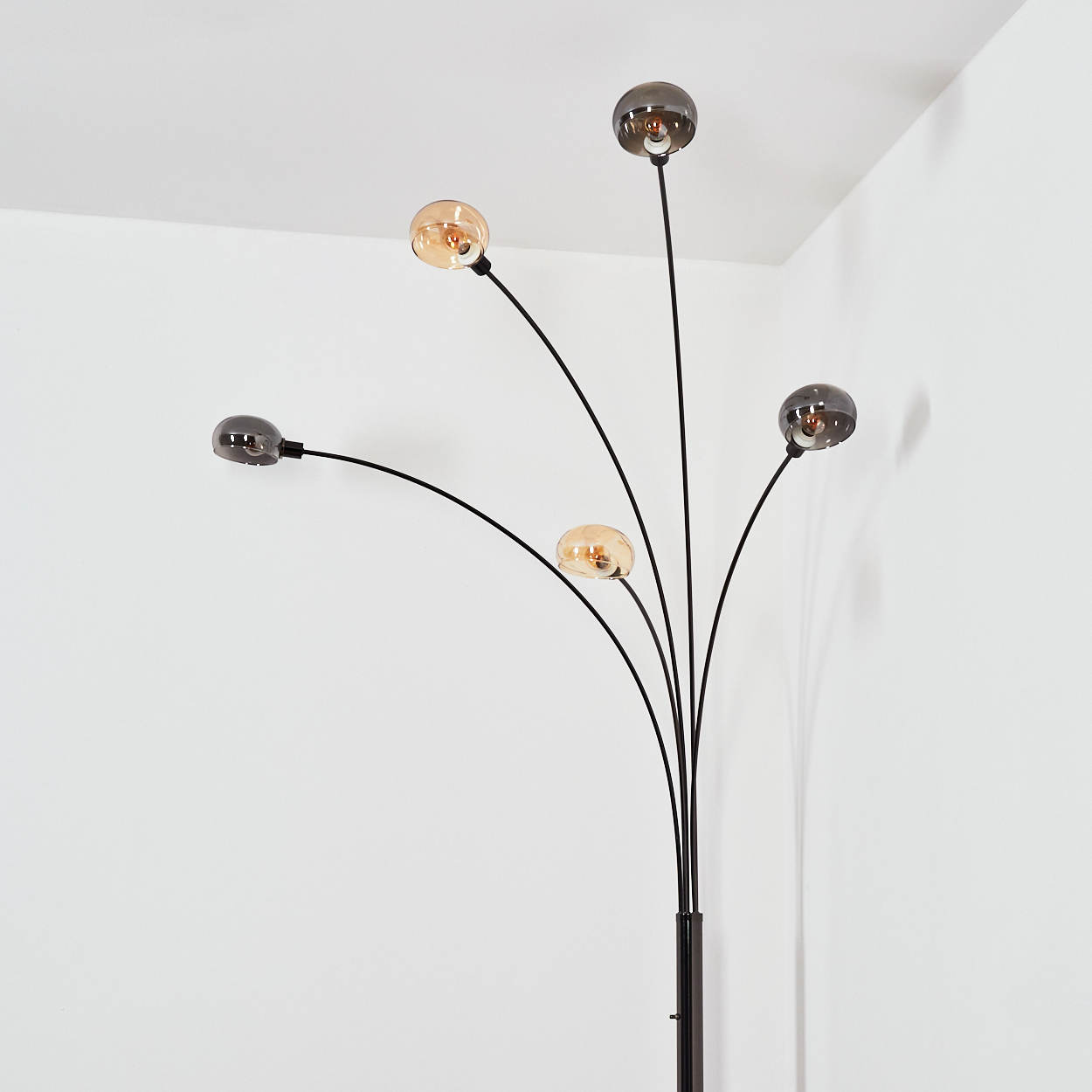 Eine moderne Stehlampe mit fünf gebogenen schwarzen Armen und kugelförmigen Glühbirnen. Der Hintergrund ist eine weiße Ecke.