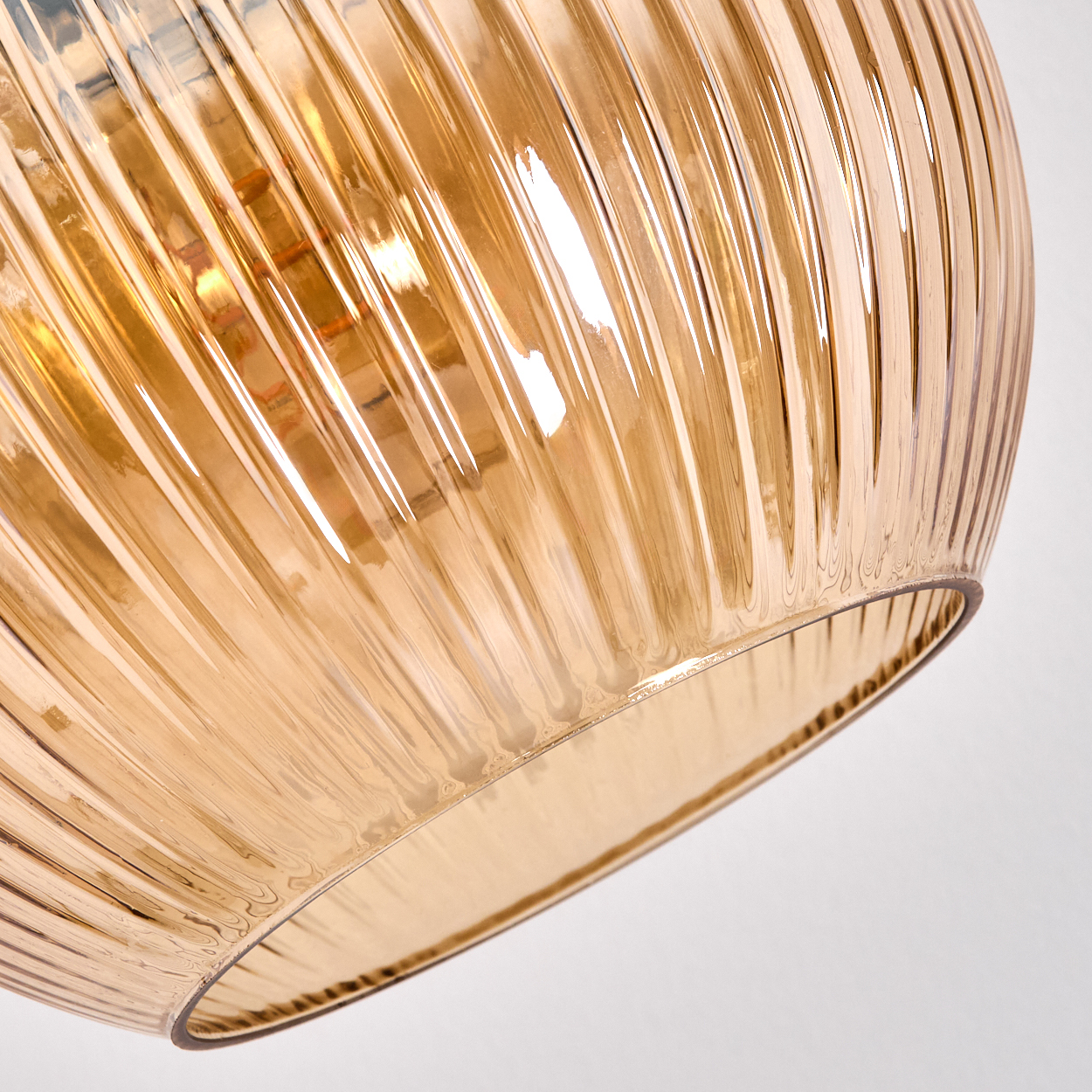 Nahaufnahme eines Lampenschirms aus Glas mit vertikalen Rippen. Er ist bernsteinfarben und teilweise transparent, mit Lichtreflexen im Inneren.