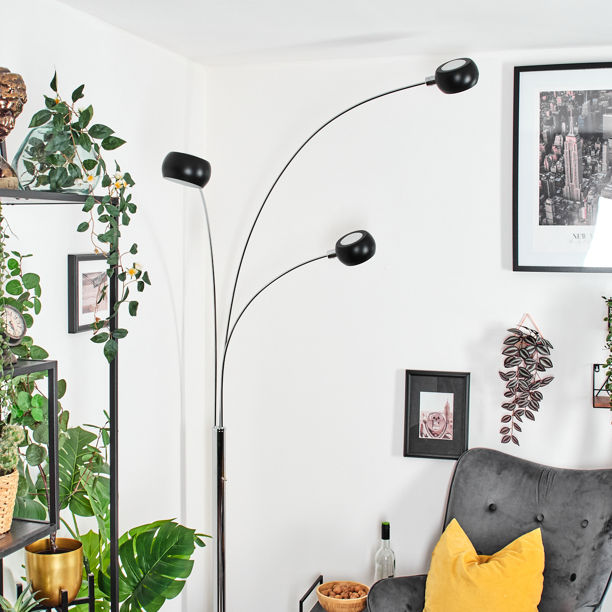 Modernes Wohnzimmer mit schwarzer Stehlampe, grauem Sessel und Pflanzen. Kunstwerke und Dekoration an den Wänden.