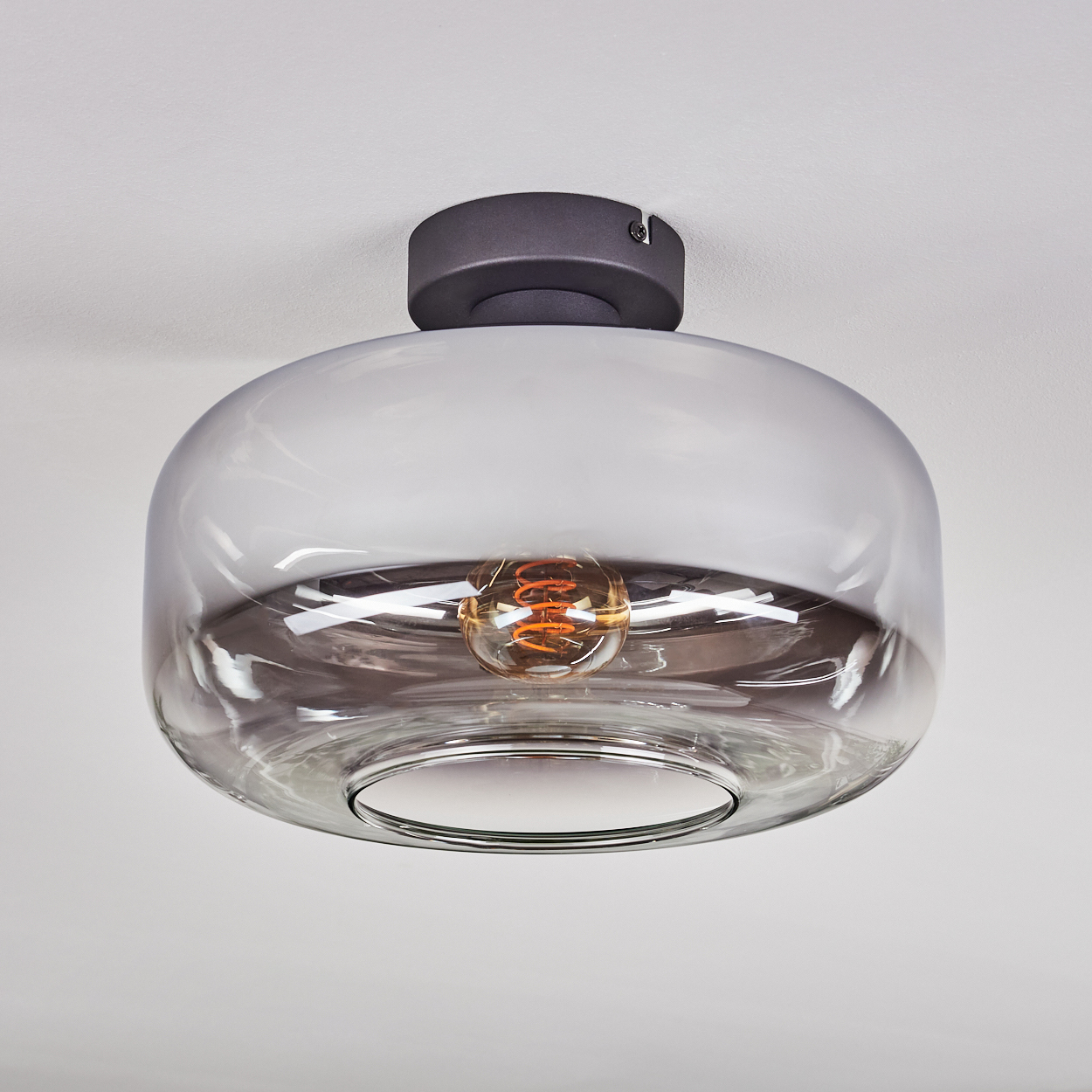 Eine moderne Deckenlampe mit klarem Glasschirm und sichtbarer, leuchtender Glühbirne.
