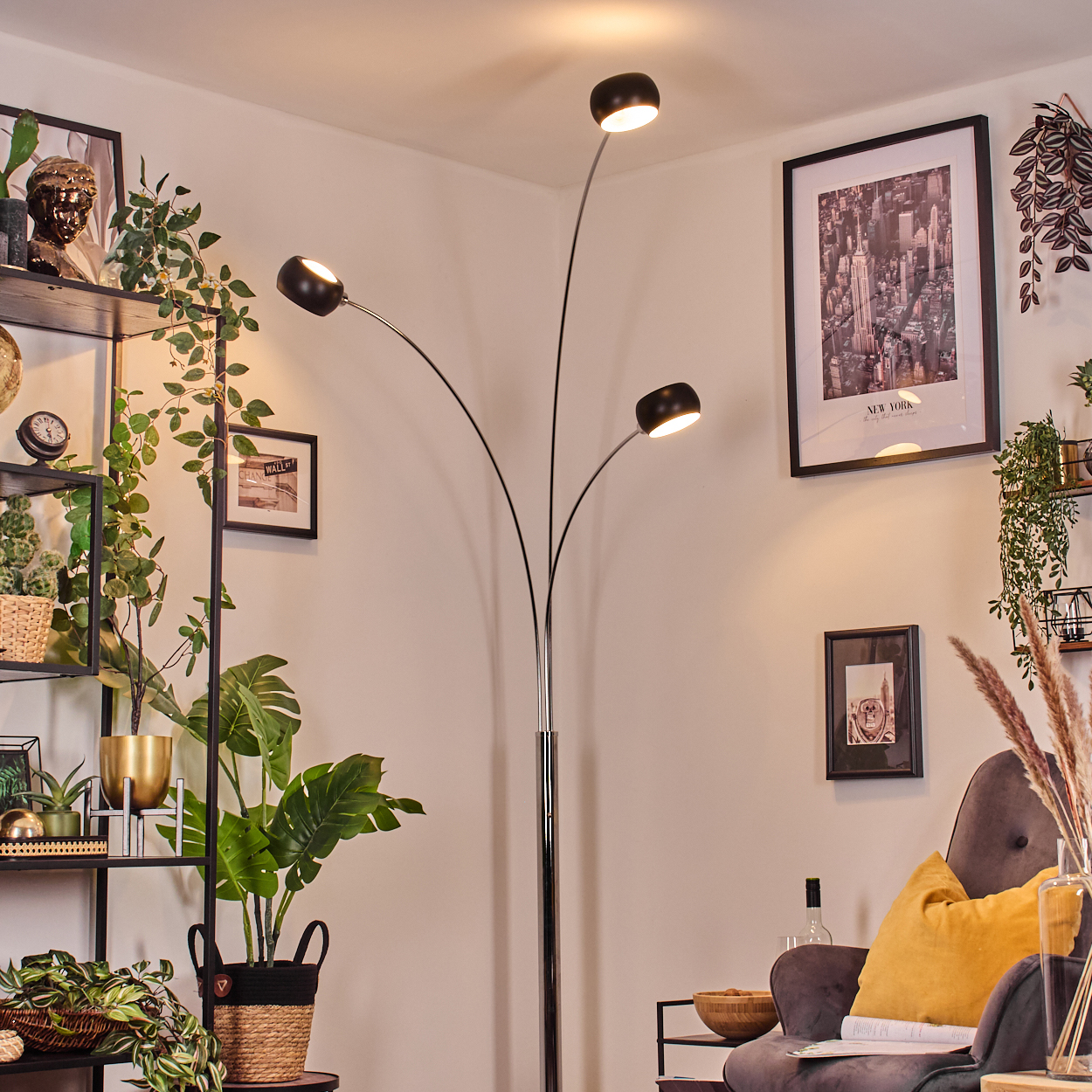Ein modernes Wohnzimmer mit Stehlampe. Es gibt ein Regal mit Pflanzen, gerahmter Kunst und einem grauen Sessel mit gelben Kissen.