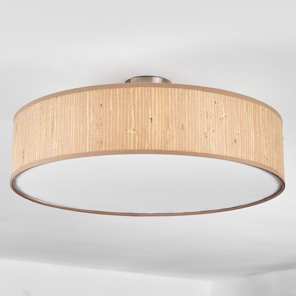 Eine Deckenleuchte. Sie hat einen gewebten beigen Schirm und einen weißen Diffusor. Der Hintergrund ist eine weiße Decke.