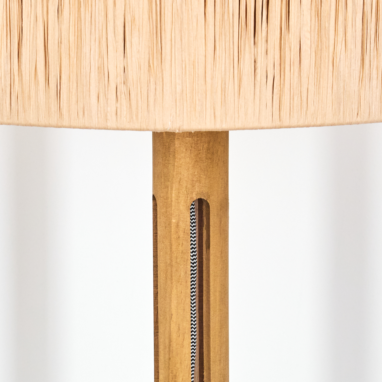 Nahaufnahme einer Lampe. Beiger Lampenschirm über einem Holzpfahl. Schwarz-weißes Zickzackmuster im Pfahl sichtbar.