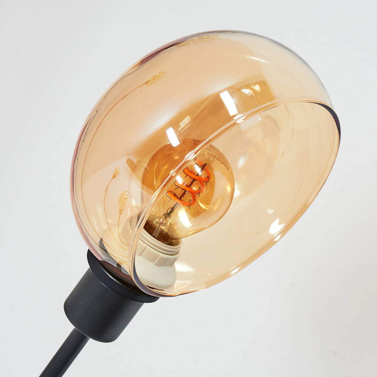 Nahaufnahme einer Lampe mit einer Glühbirne in einem bernsteinfarbenen Glasschirm auf weißem Hintergrund.