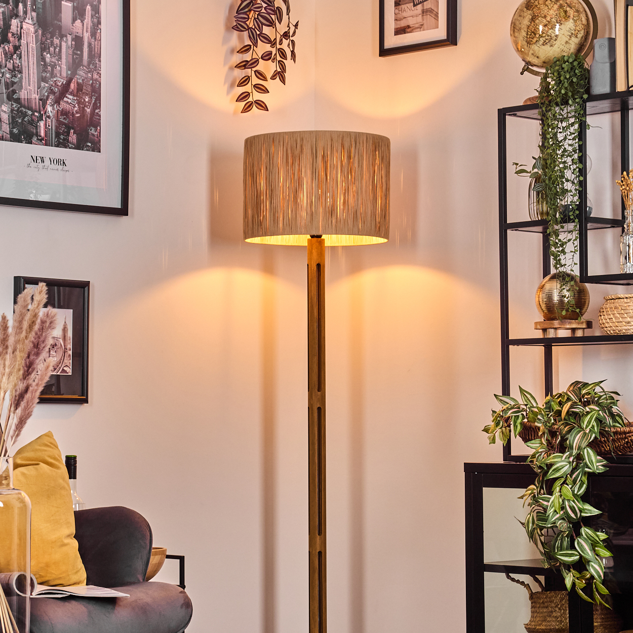 Ein Raum mit Stehlampe, Wandkunst, Regal mit Pflanzen, Stuhl und Globus. Die Lampe hat einen beigen Schirm.
