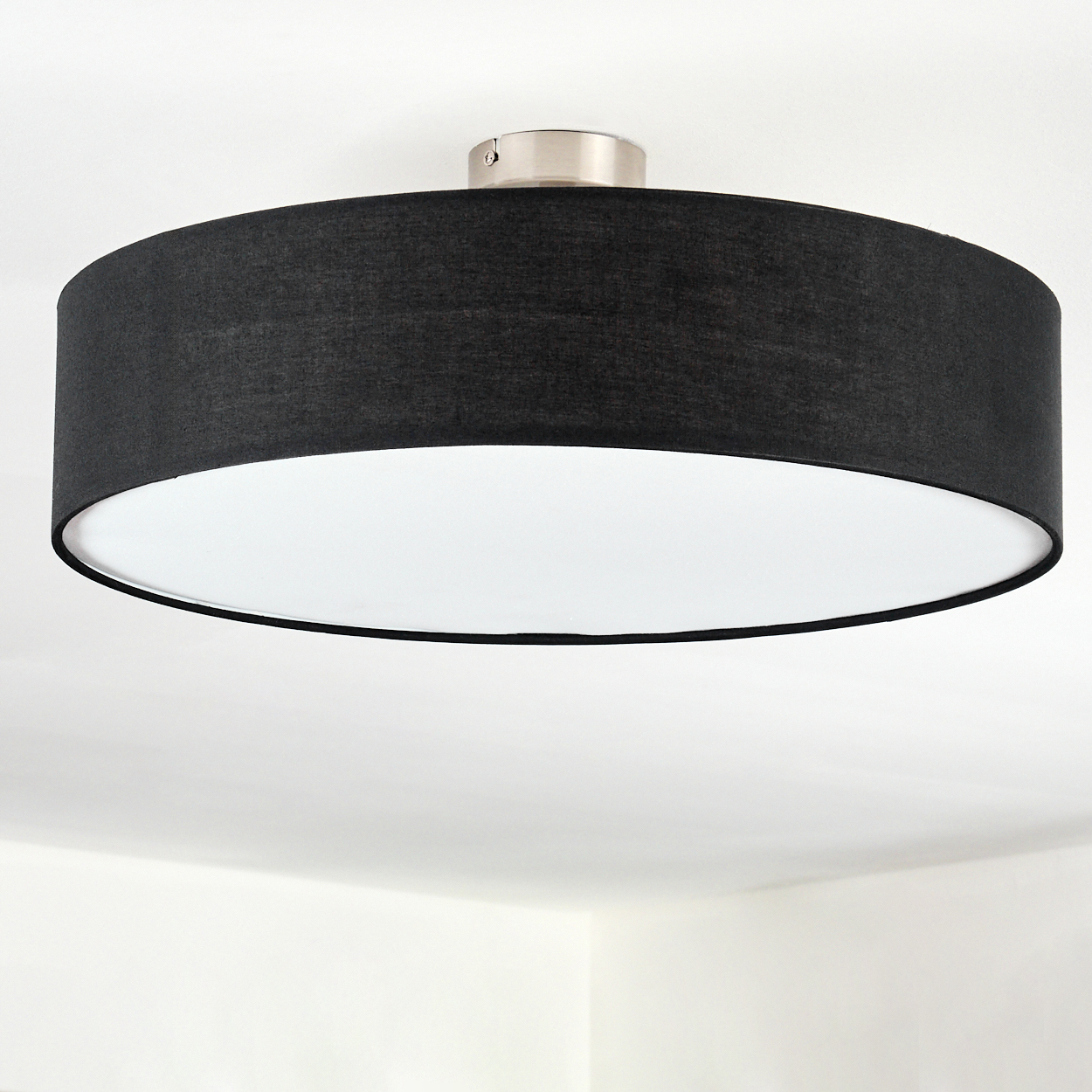 Eine moderne Deckenlampe. Sie hat einen schwarzen Schirm und ein weißes Innere. Die Lampe ist an einer weißen Decke montiert.