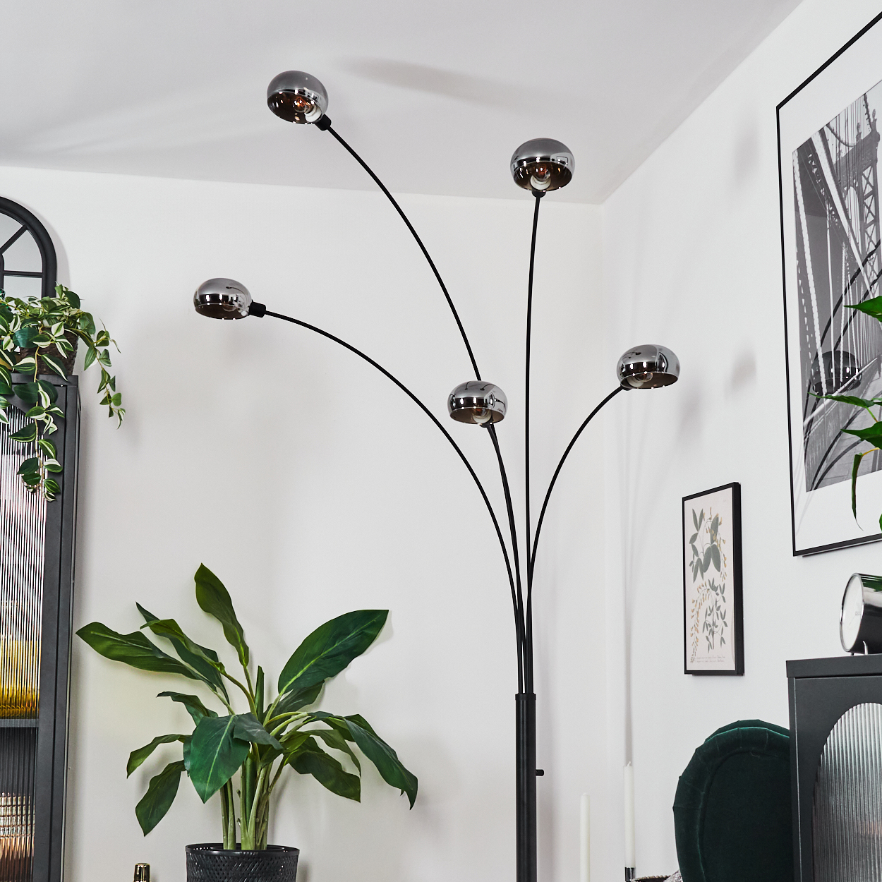 Ein modernes Wohnzimmer mit einer schwarzen Stehlampe mit fünf kugelförmigen Lampenschirmen, einer großen Pflanze und Kunstwerken an der Wand.