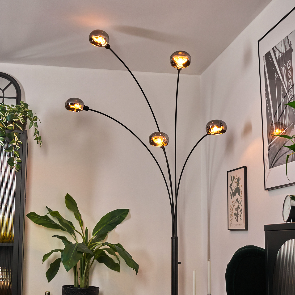 Eine moderne Stehlampe mit fünf Glühbirnen, Pflanzen, einem gerahmten Bild, einem schwarzen Schrank und einem grünen Stuhl.