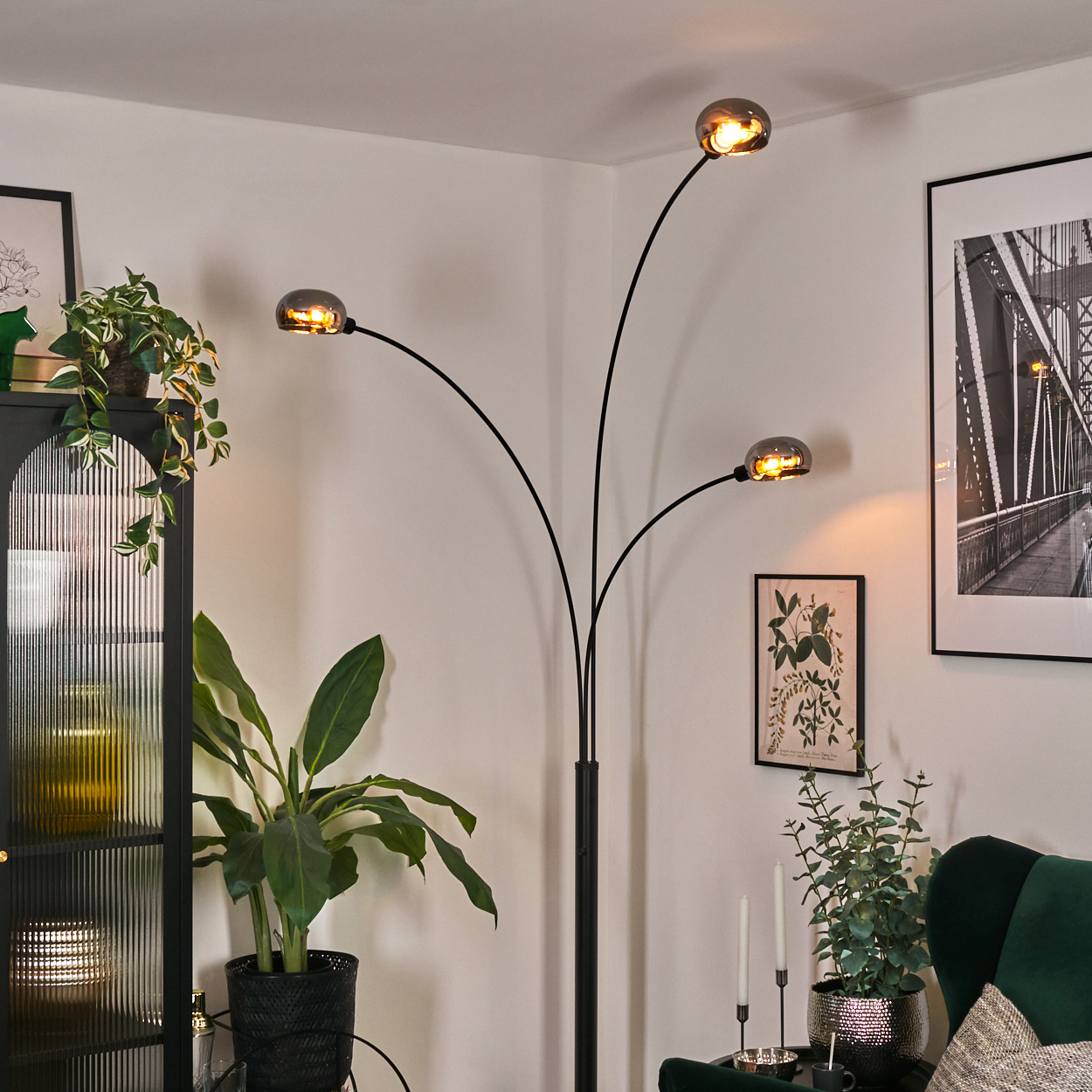 Modernes Wohnzimmer mit schwarzer Stehlampe, Pflanzen, Gemälde und grünem Sessel.