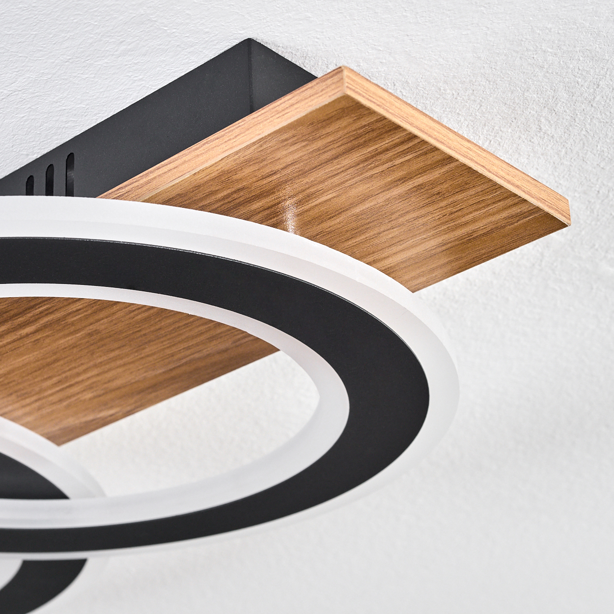 Nahaufnahme einer modernen Deckenleuchte. Sie hat ein Holzregal, schwarz-weiße kreisförmige Lichter und einen weißen Deckenhintergrund.