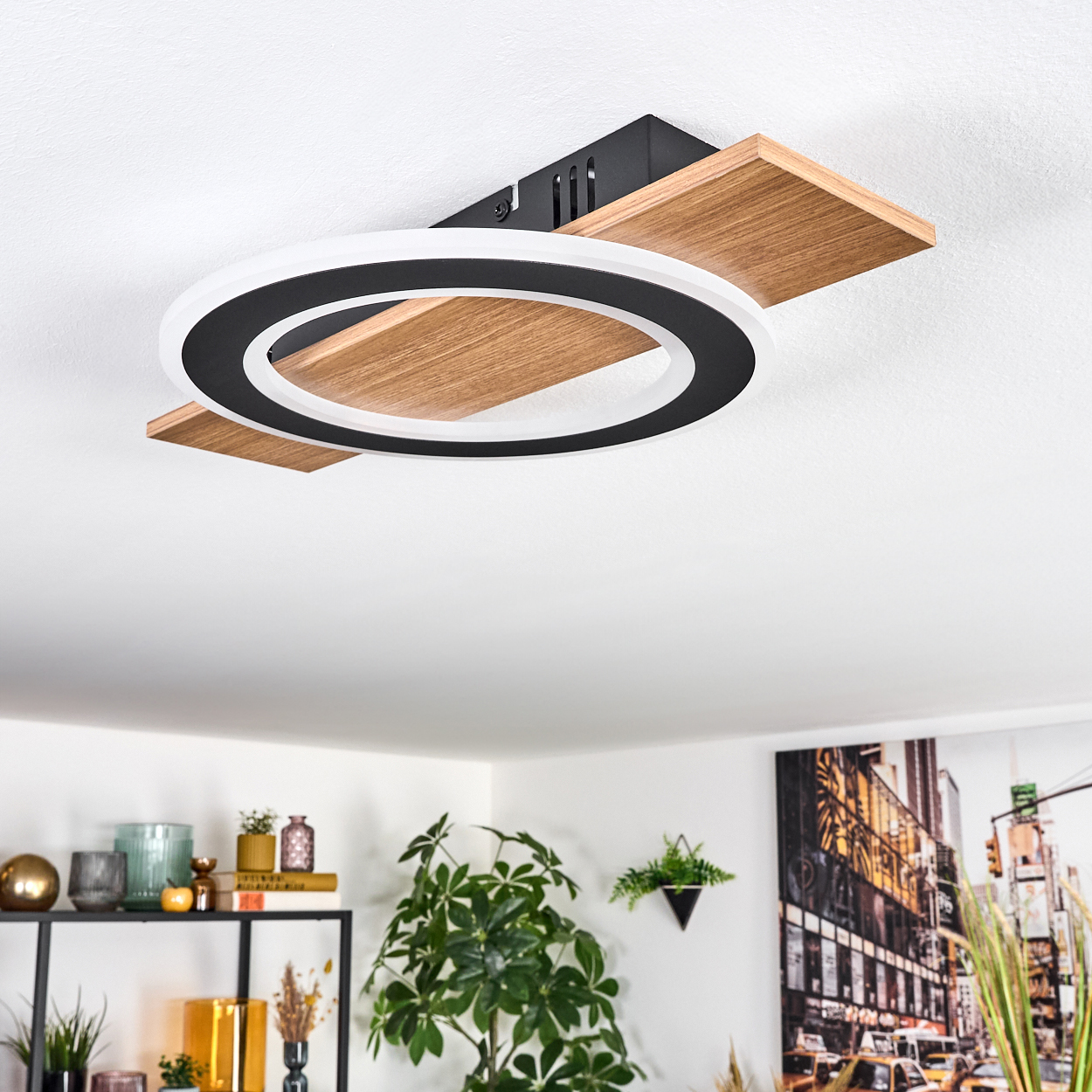 Eine moderne Deckenleuchte mit einem schwarz-weißen kreisförmigen Design. Sie ist an einer weißen Decke installiert. Regale und Pflanzen sind im Hintergrund.