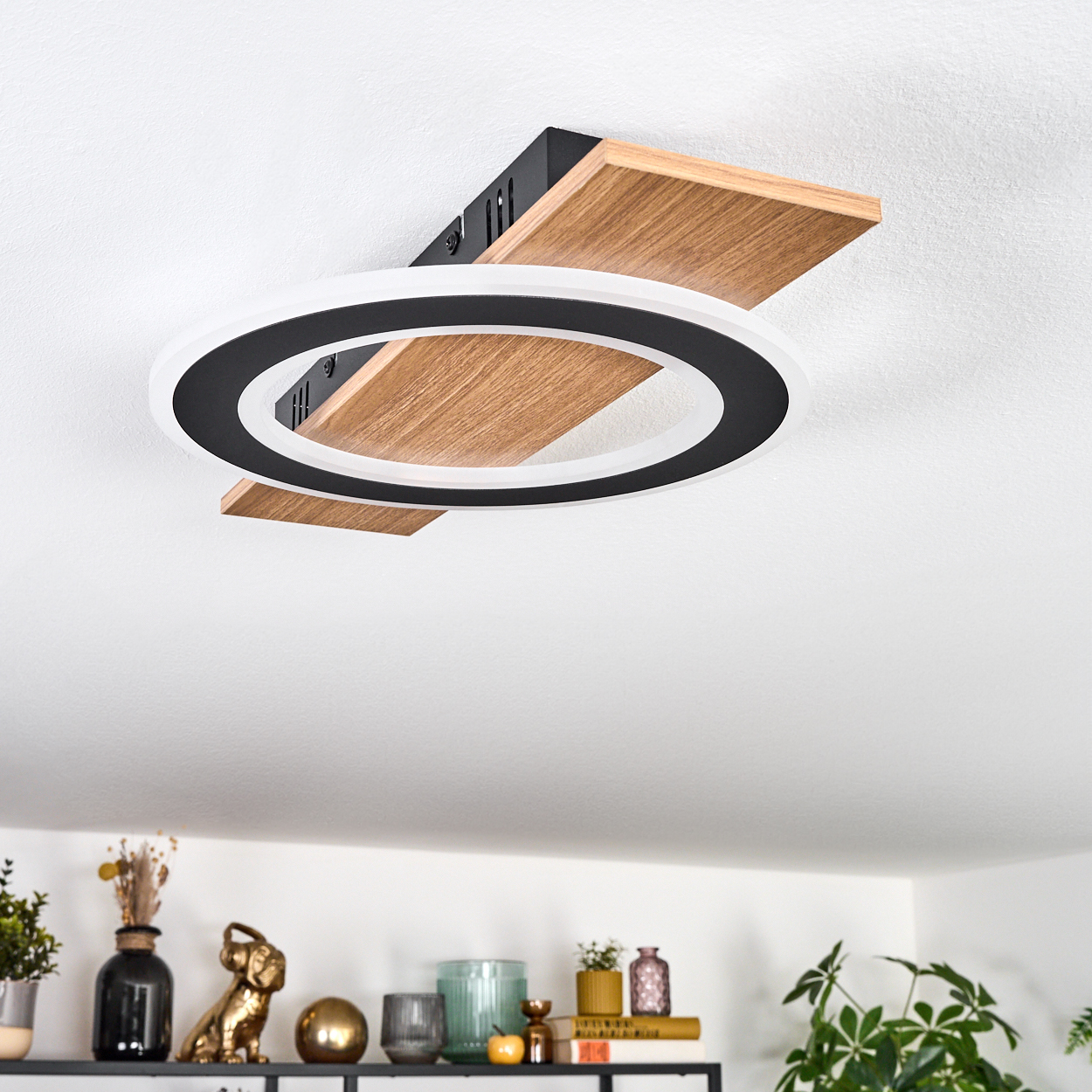 Eine moderne Deckenlampe mit Holzsockel und schwarzem und weißem Kreislicht. Darunter ein Regal mit verschiedenen Dekorationsartikeln.