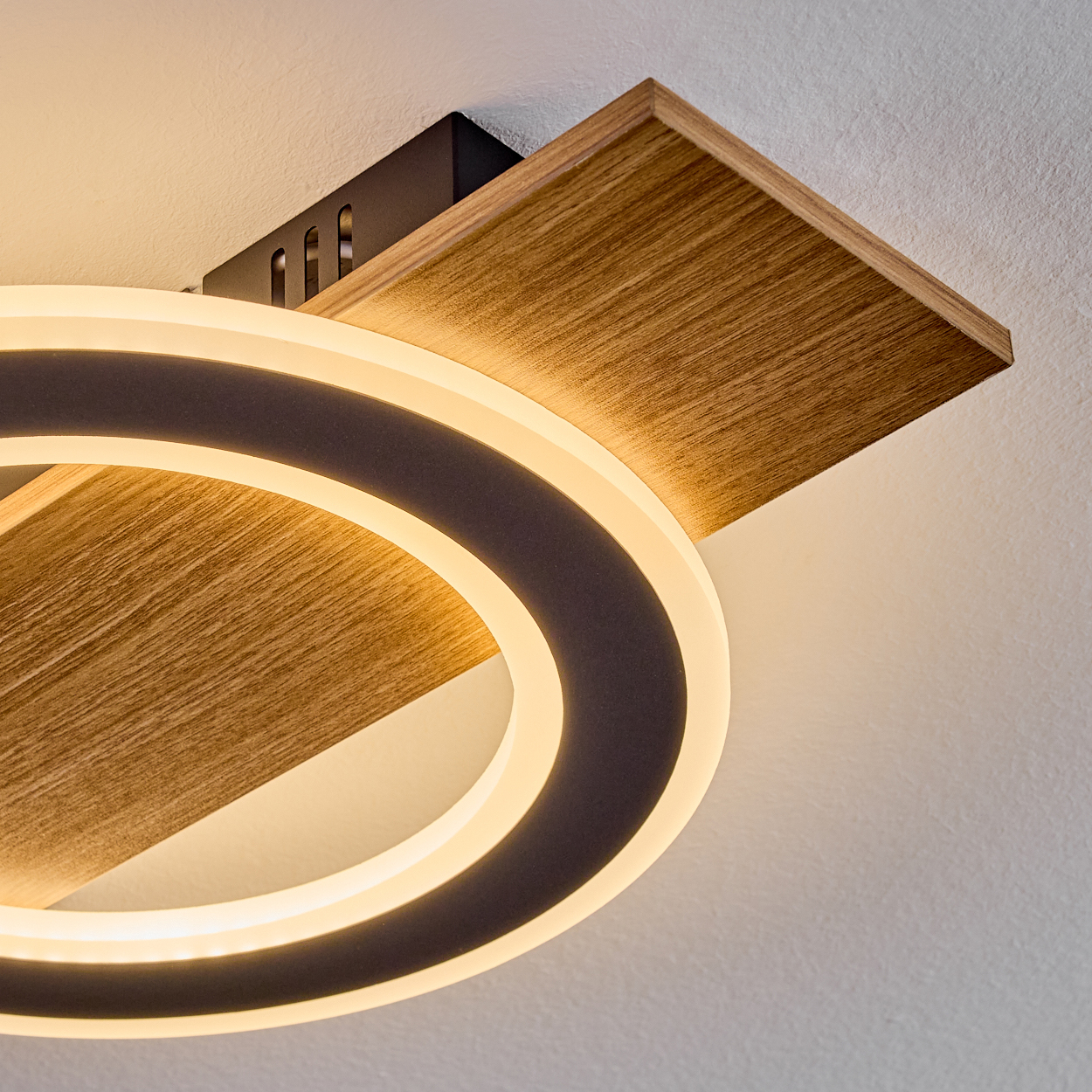 Moderne Deckenleuchte. Sie hat ein kreisförmiges Licht und eine Holzplatte, alles vor einer weißen Decke.