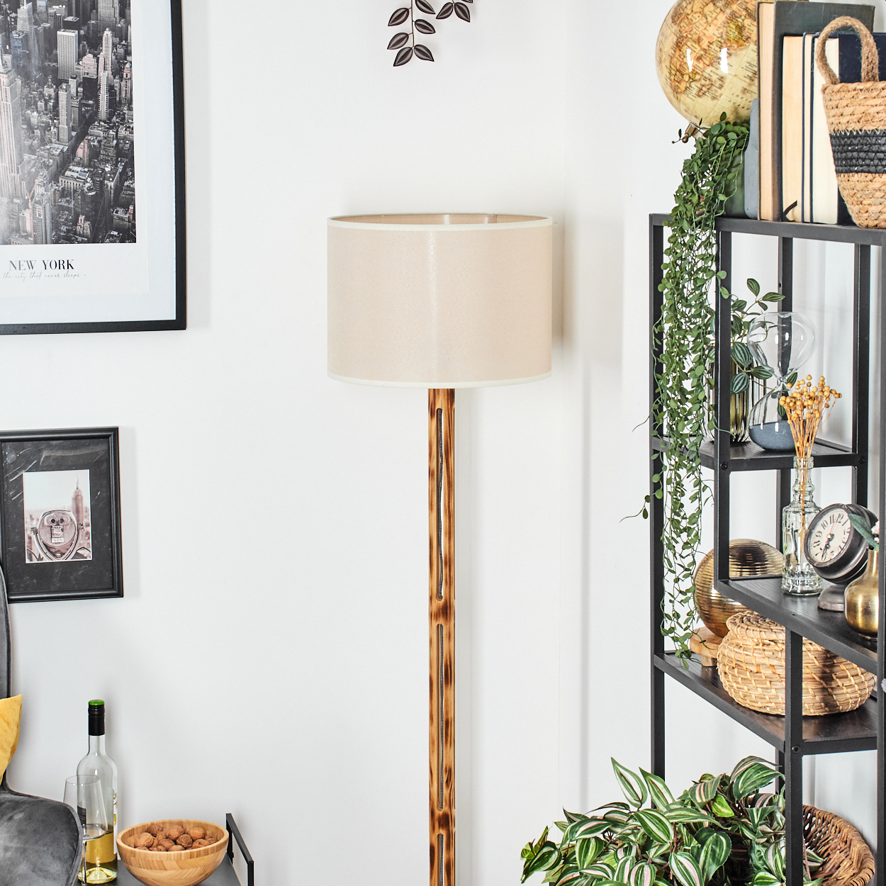 Ein Raum mit Stehlampe, Regal mit Büchern und Dekorationen und gerahmten Bildern. Eine Schale mit Walnüssen steht auf einem Tisch.