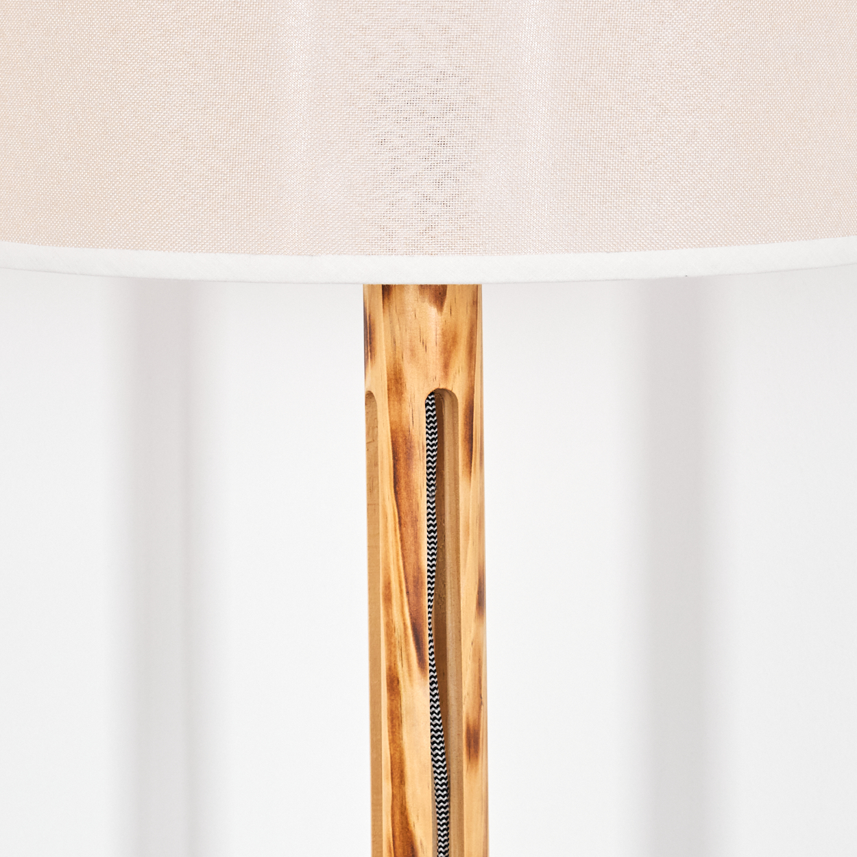 Nahaufnahme einer Lampe. Beiger Lampenschirm auf einem Holzpfosten mit einem schwarz-weißen Kabel in der Mitte. Weißer Hintergrund.