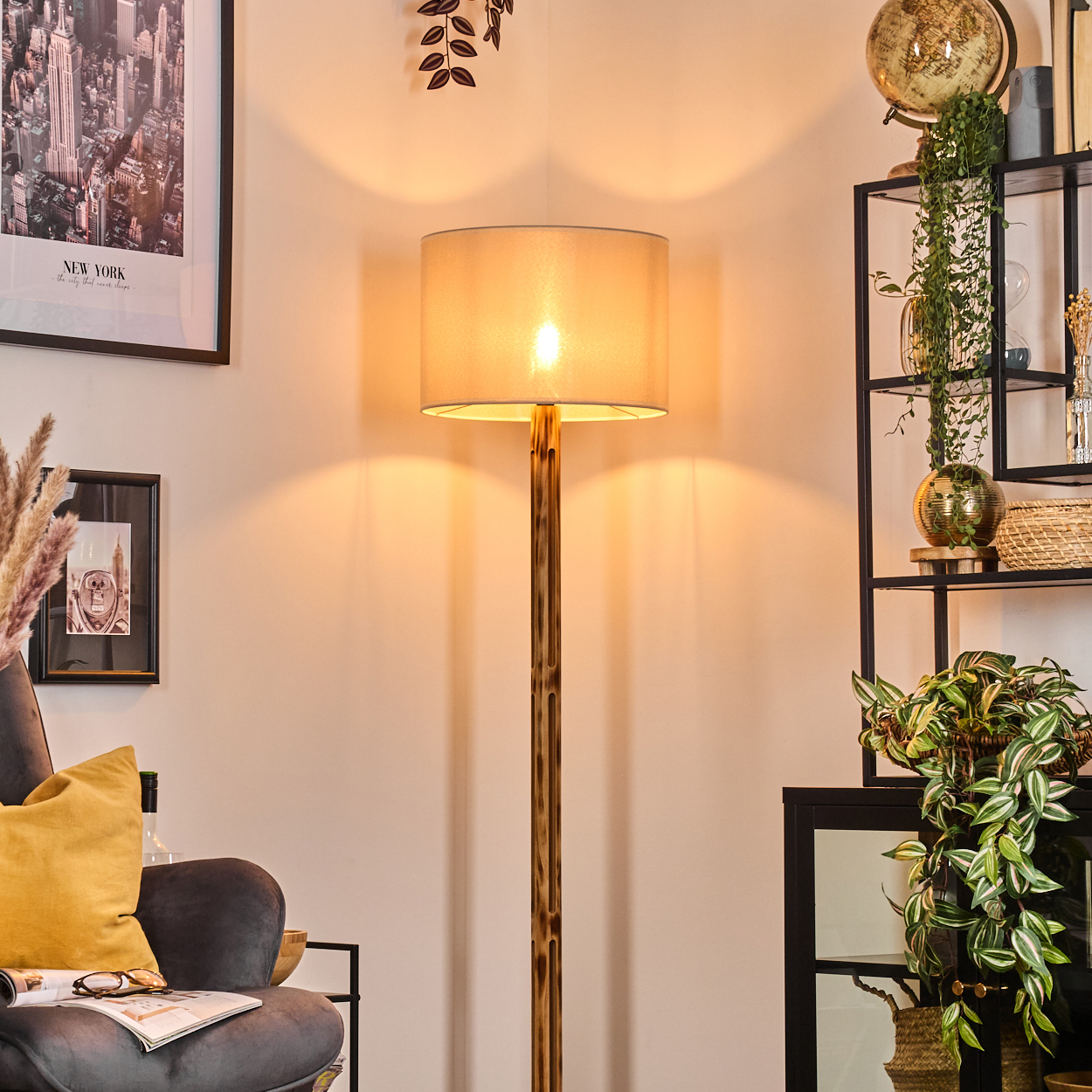 Eine beleuchtete Lampe ist der Mittelpunkt. Ein New York-Bild hängt an der Wand, mit einem grauen Sessel und einem Regal mit Pflanzen.