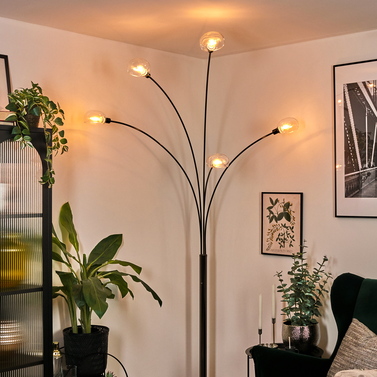 Ein modernes Wohnzimmer mit einer schwarzen Stehlampe mit fünf Glühbirnen, Pflanzen, einem gerahmten Brückenfoto und einem dunkelgrünen Sessel.