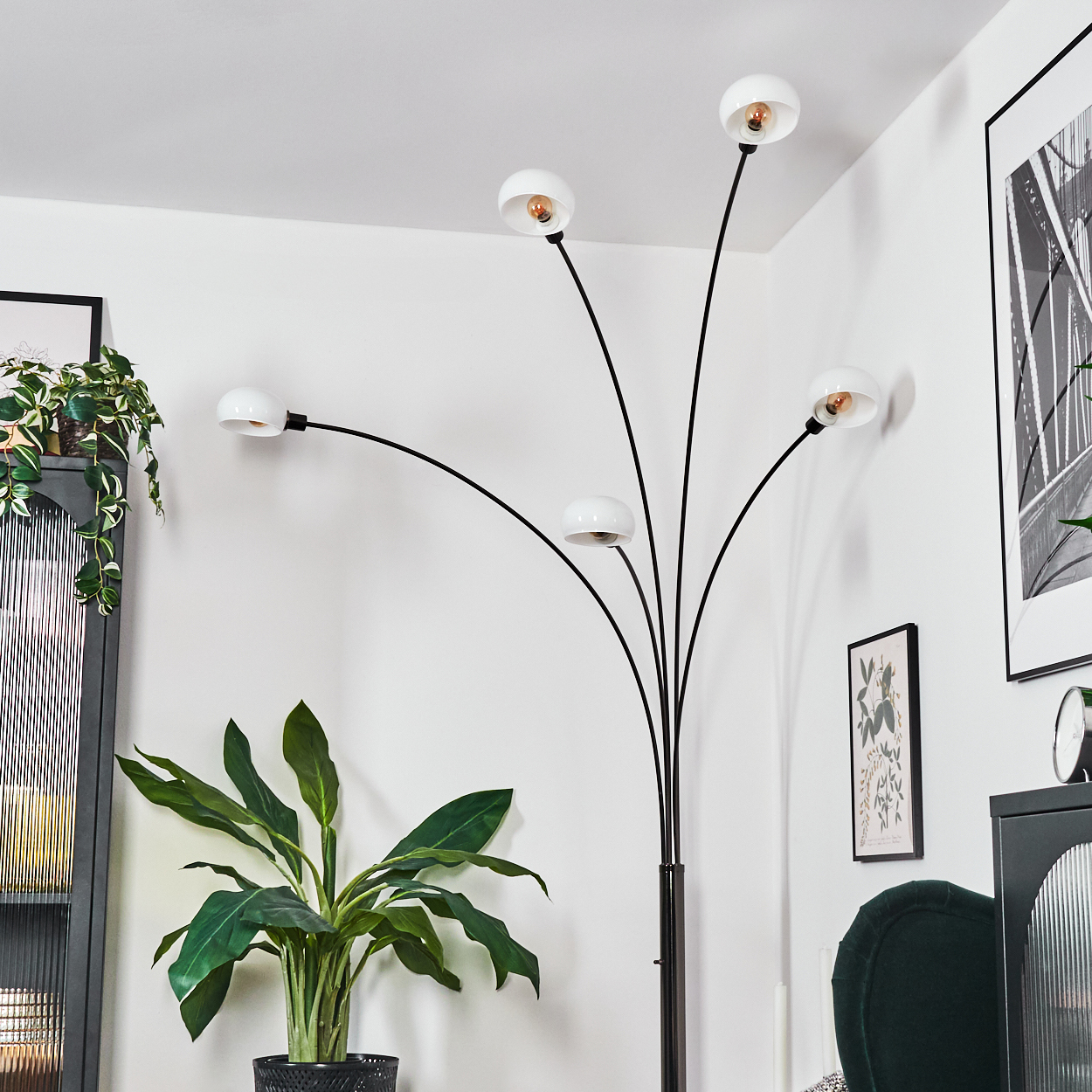 Ein modernes Wohnzimmer mit einer hohen schwarzen Lampe mit weißen Kugeln, einer großen Topfpflanze und gerahmten Kunstwerken an weißen Wänden.
