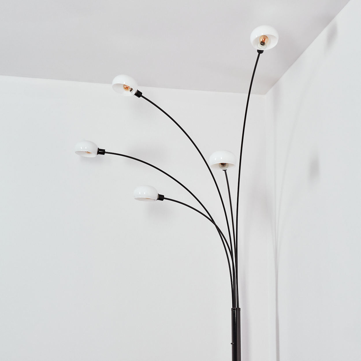 Eine moderne Stehlampe mit fünf weißen Lampenschirmen an schwarzen, gebogenen Armen. Die Lampe steht in einer weißen Ecke.