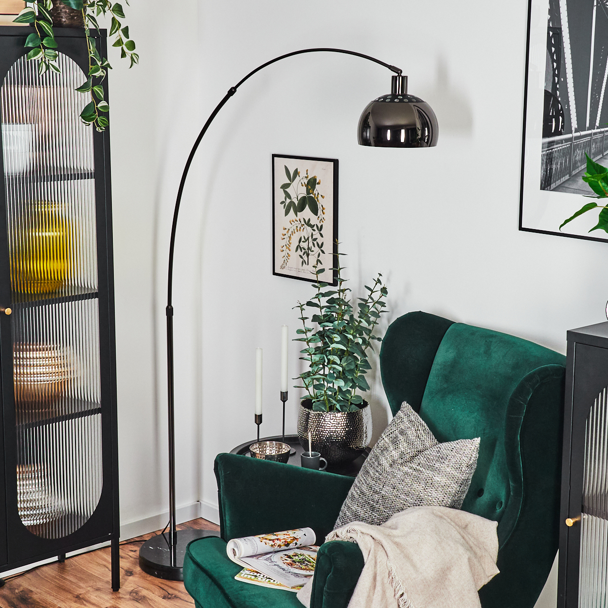 Ein grüner Sessel mit Kissen, eine schwarze Lampe, ein Schrank und eine Pflanze. Ein Bild hängt an der Wand.