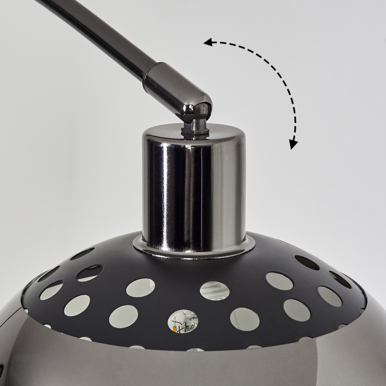 Nahaufnahme einer Lampe. Schwarzer Schirm mit Löchern, Chromfuß und verstellbarem Arm. Pfeil zeigt die Bewegung. Weißer Hintergrund.