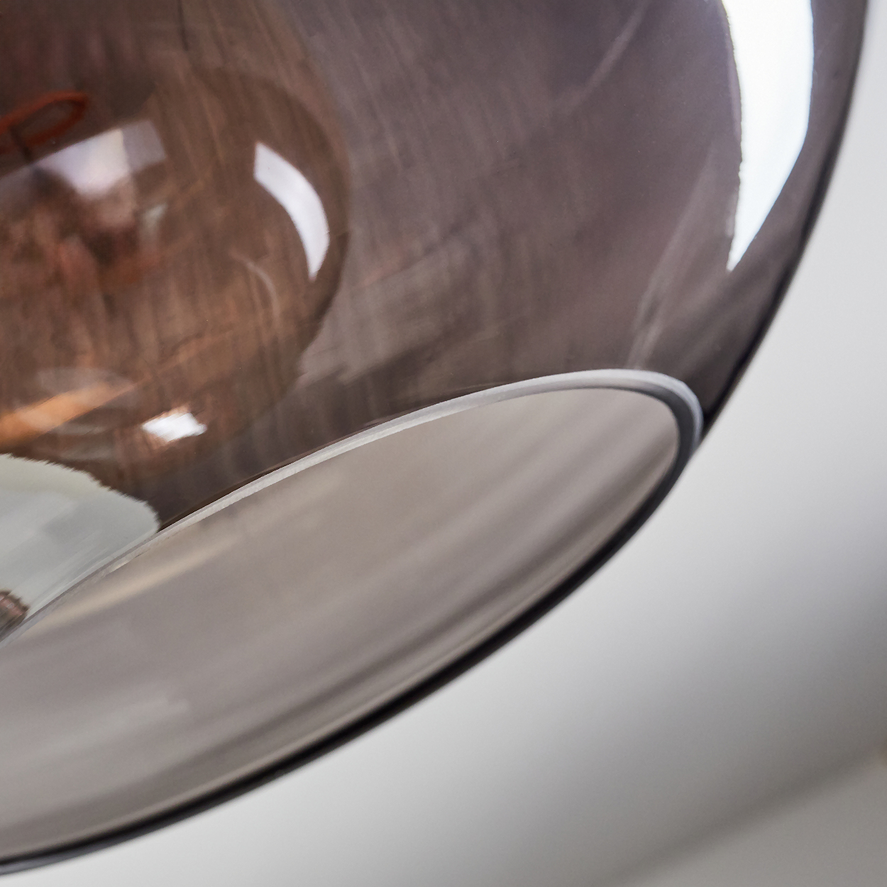 Nahaufnahme eines Glasschirms mit dunkler, rauchiger Tönung. Das Glas reflektiert Licht und Umgebung, vor weißem Hintergrund.